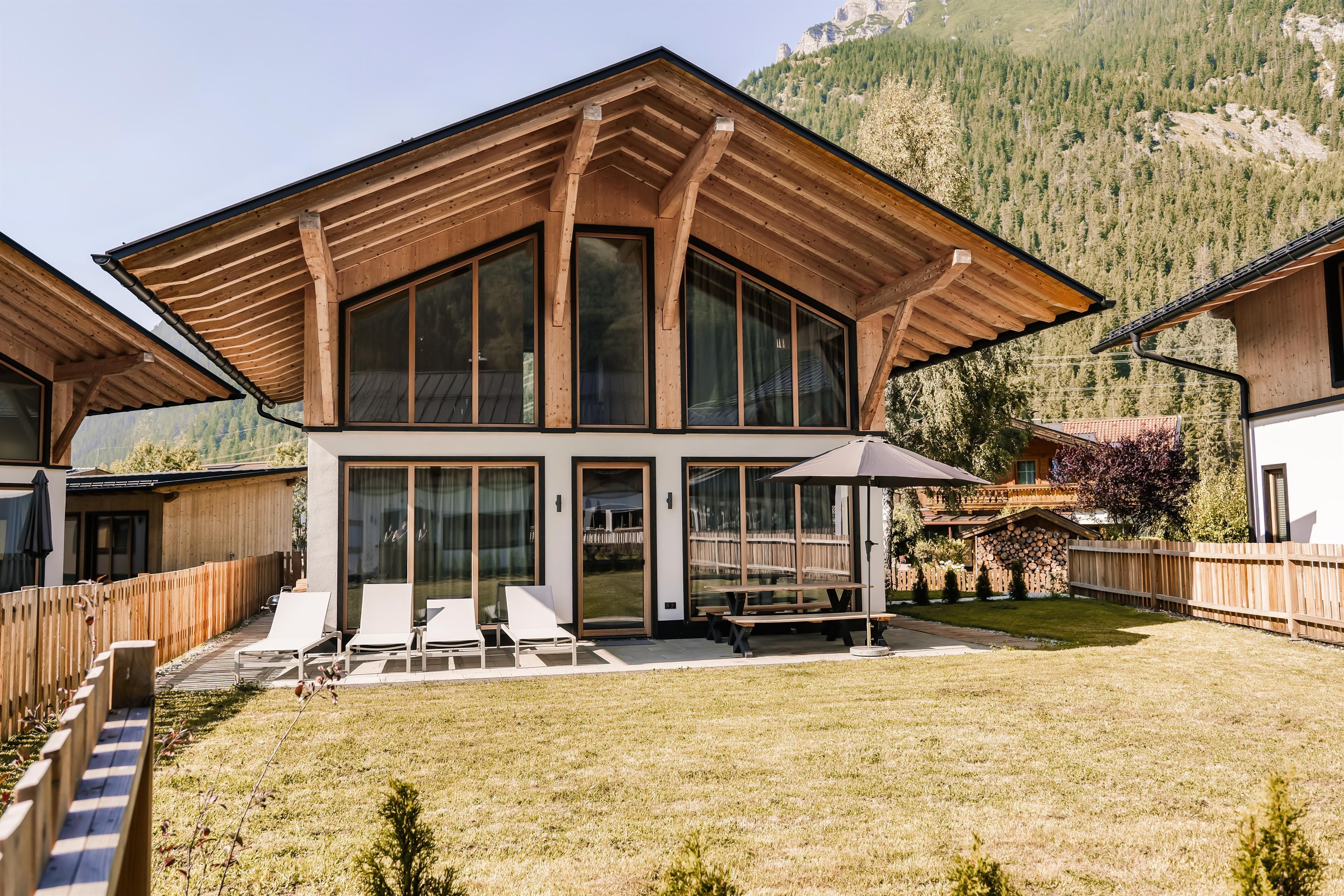A modern house with a distinctive roof and large windows. It is situated in a green environment with a well-maintained garden.