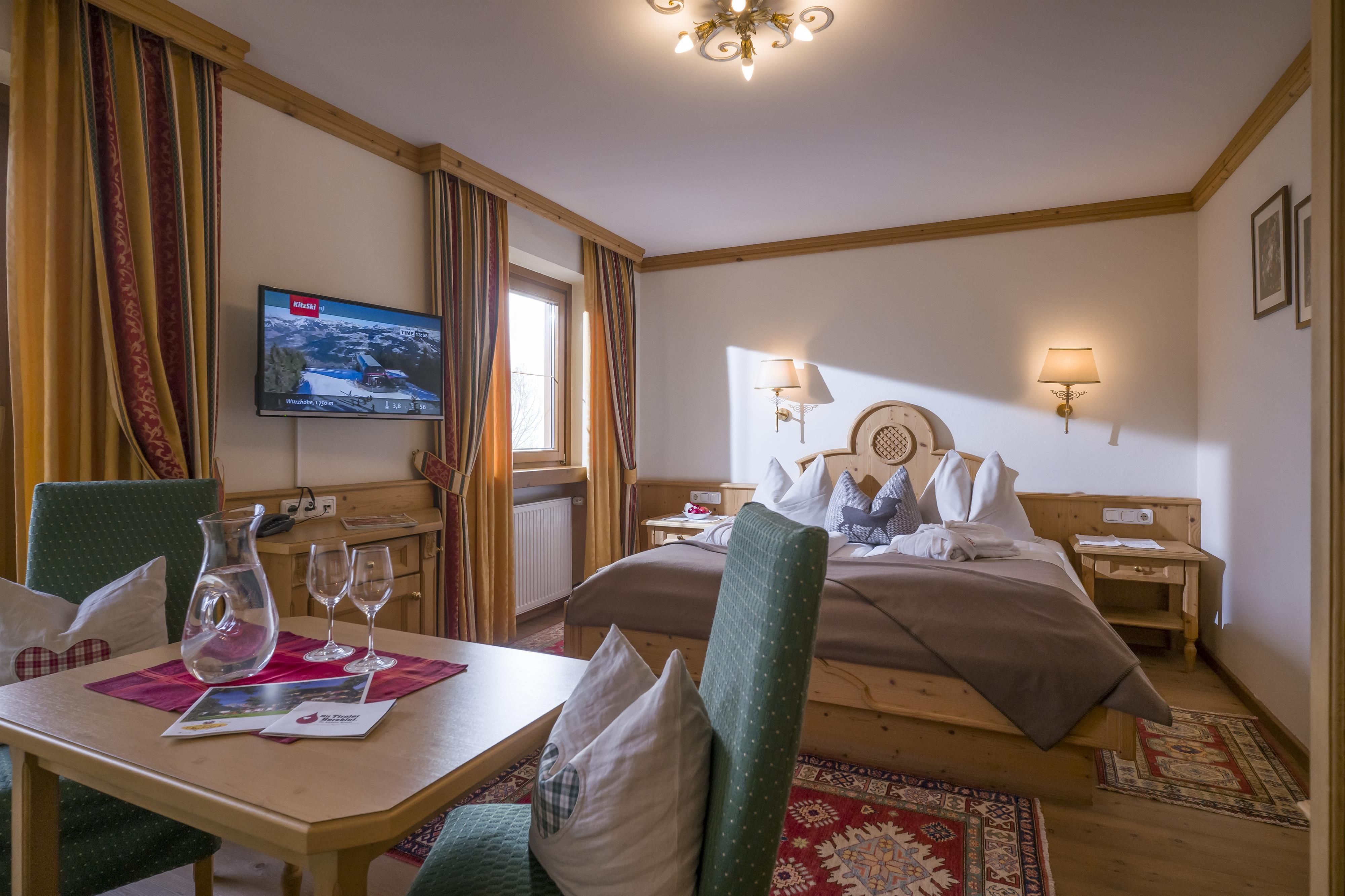 A cozy hotel room with a double bed and stylish decor. A table with glasses and a carafe complements the atmosphere.