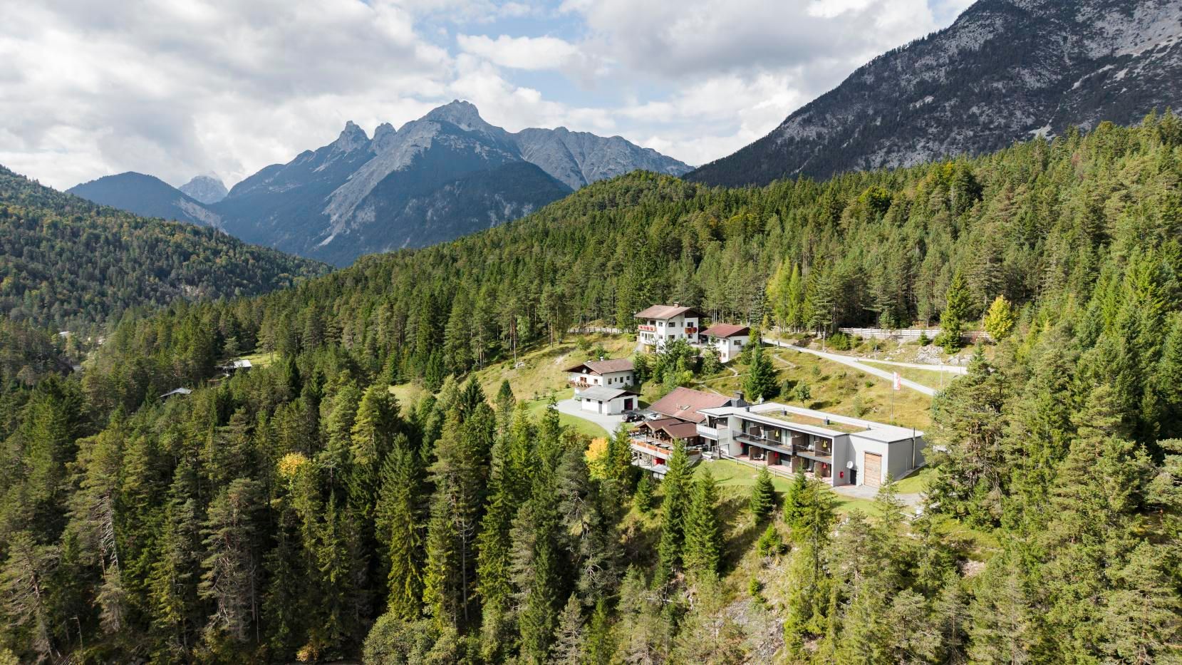 A picturesque landscape with green forests and majestic mountains in the background. In the foreground, some houses are visible, harmoniously integrated into nature.