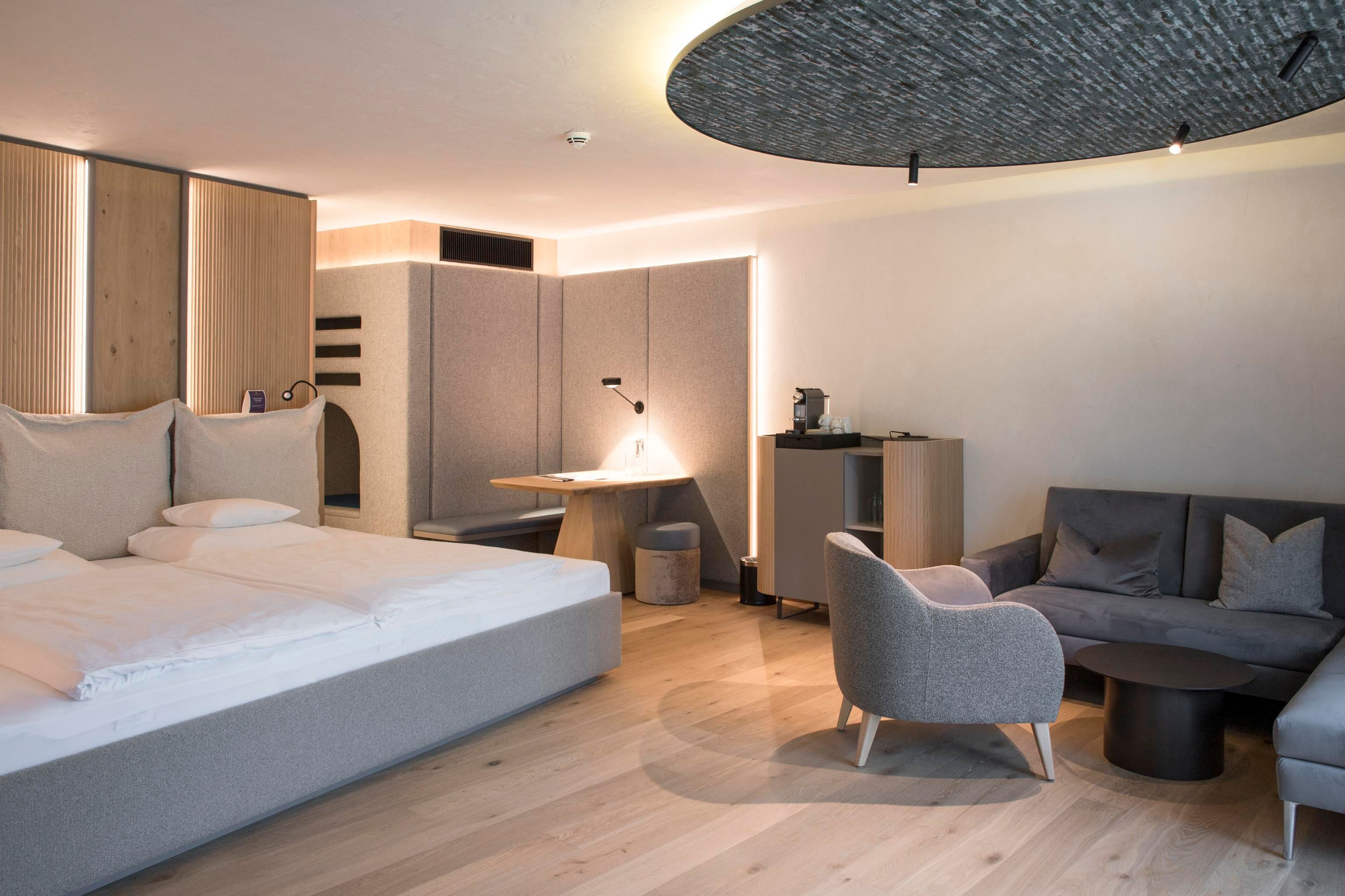 A modern hotel room with a spacious bed and a cozy seating area. The decor is bright and elegant, featuring a warm wooden floor and stylish furniture.