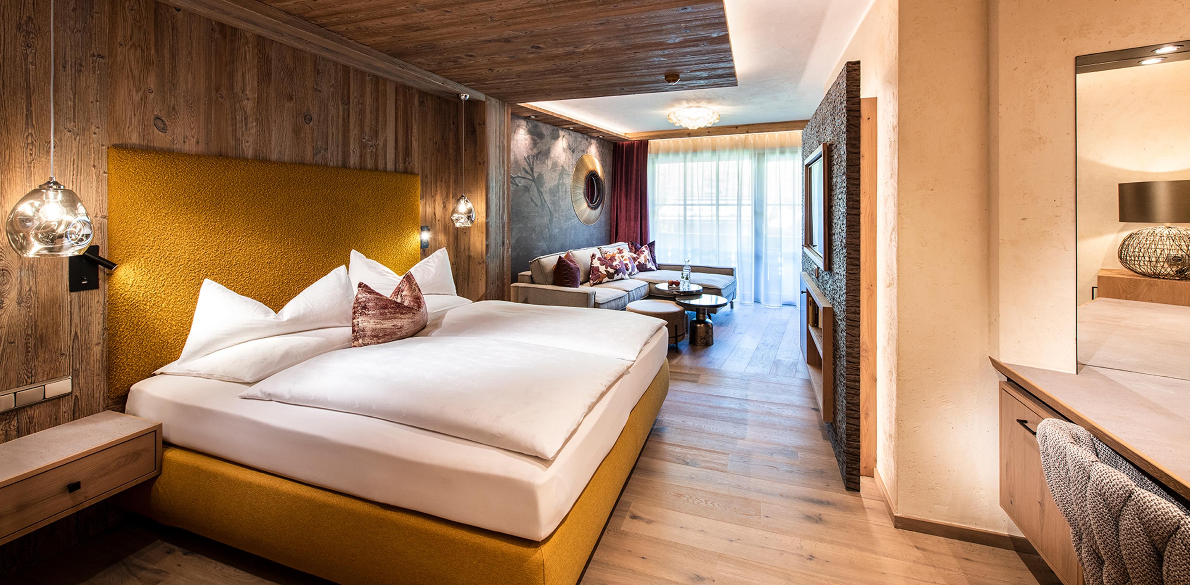 A modern hotel room with a large, comfortable bed and warm wooden details. The room offers plenty of natural light and a cozy seating area.