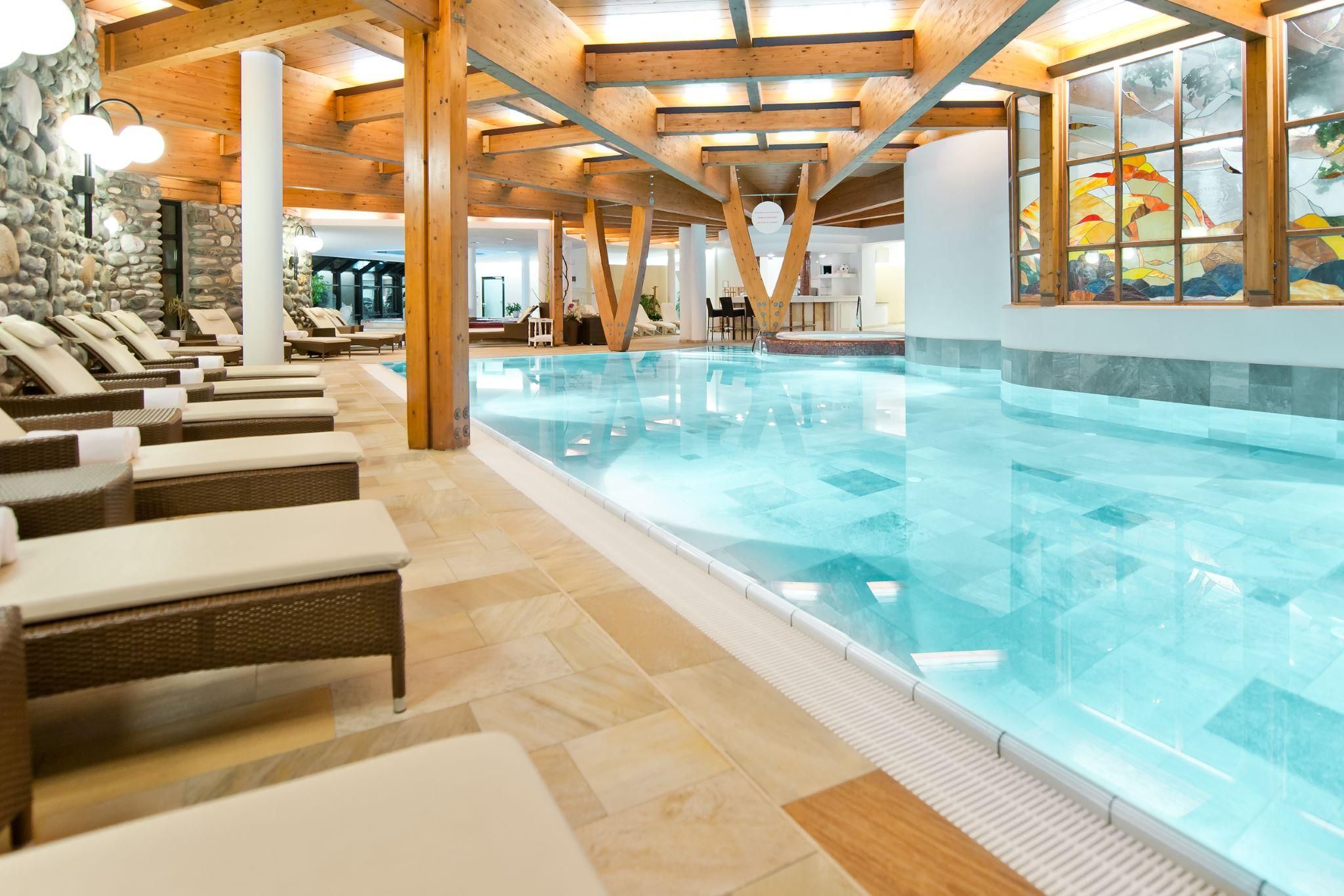 A relaxing pool area with comfortable loungers and warm wooden interior. The clear water and soft lighting create a calm atmosphere.