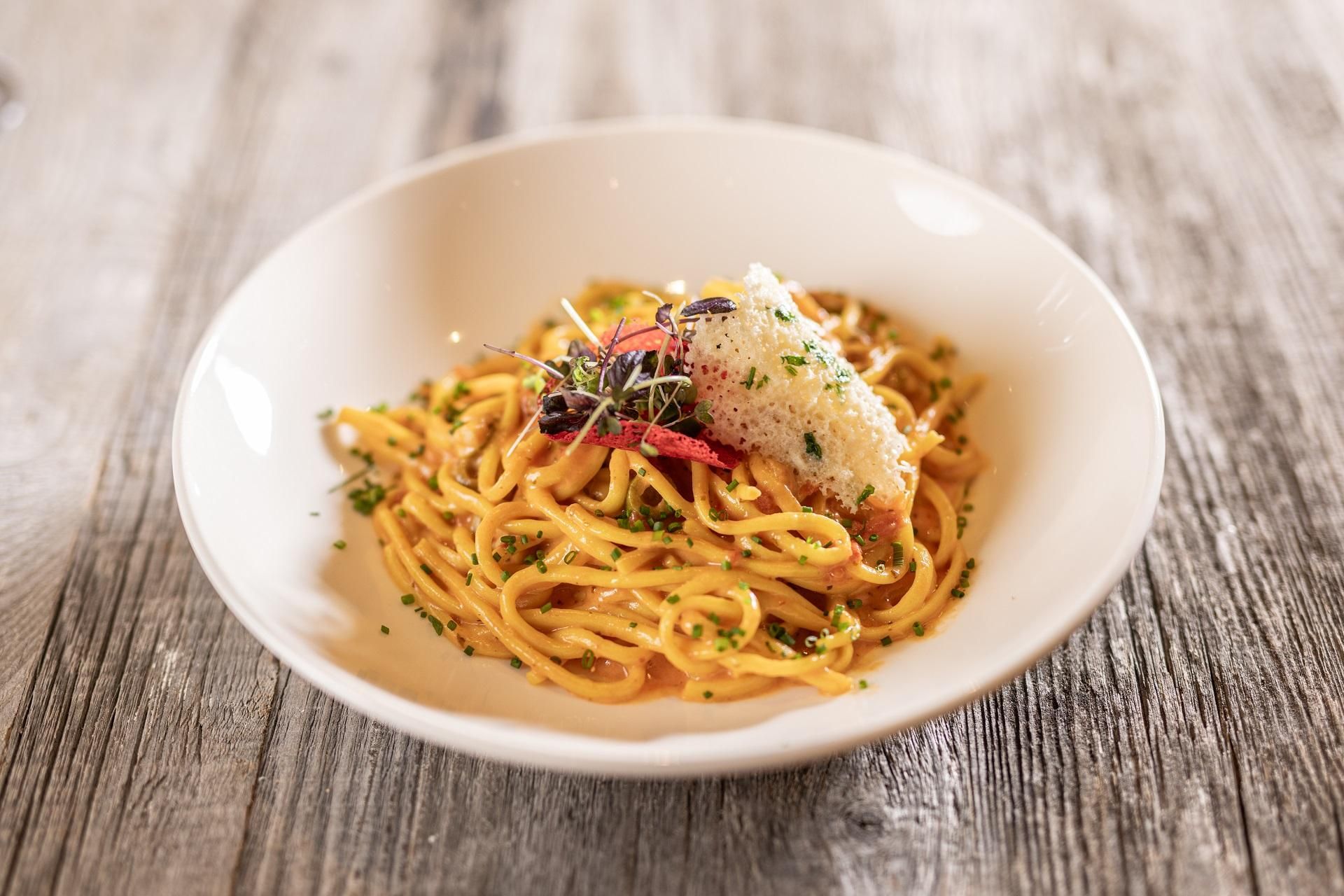 A plate of pasta, garnished with fresh herbs and cheese. The background is made of wood, creating a warm atmosphere.