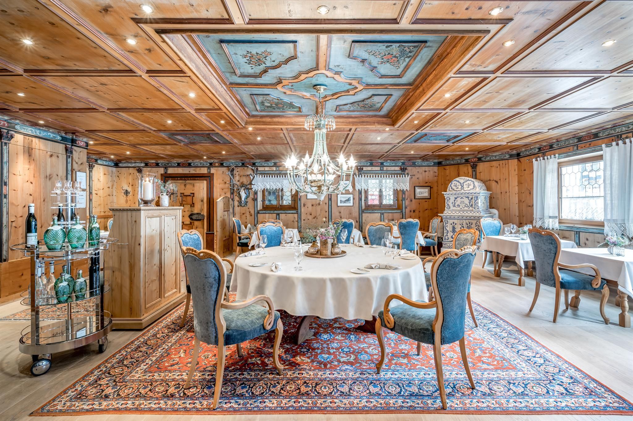 An elegant restaurant with wooden walls and an artistic ceiling pattern. A round table with decorative dishes and stylish chairs invites you to dine.