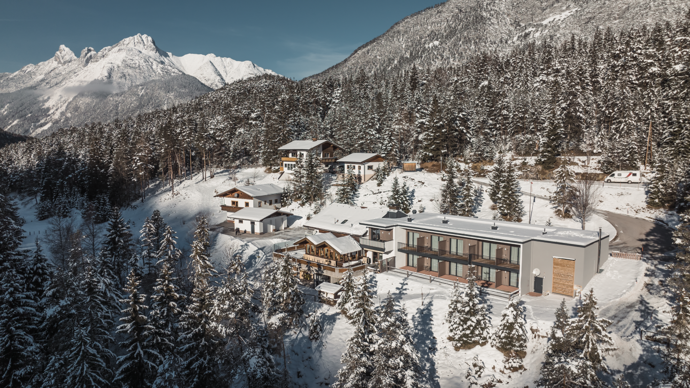 A picturesque mountain village in winter, surrounded by snow-covered fir trees. In the foreground, a modern building can be seen, nestled in the alpine landscape.