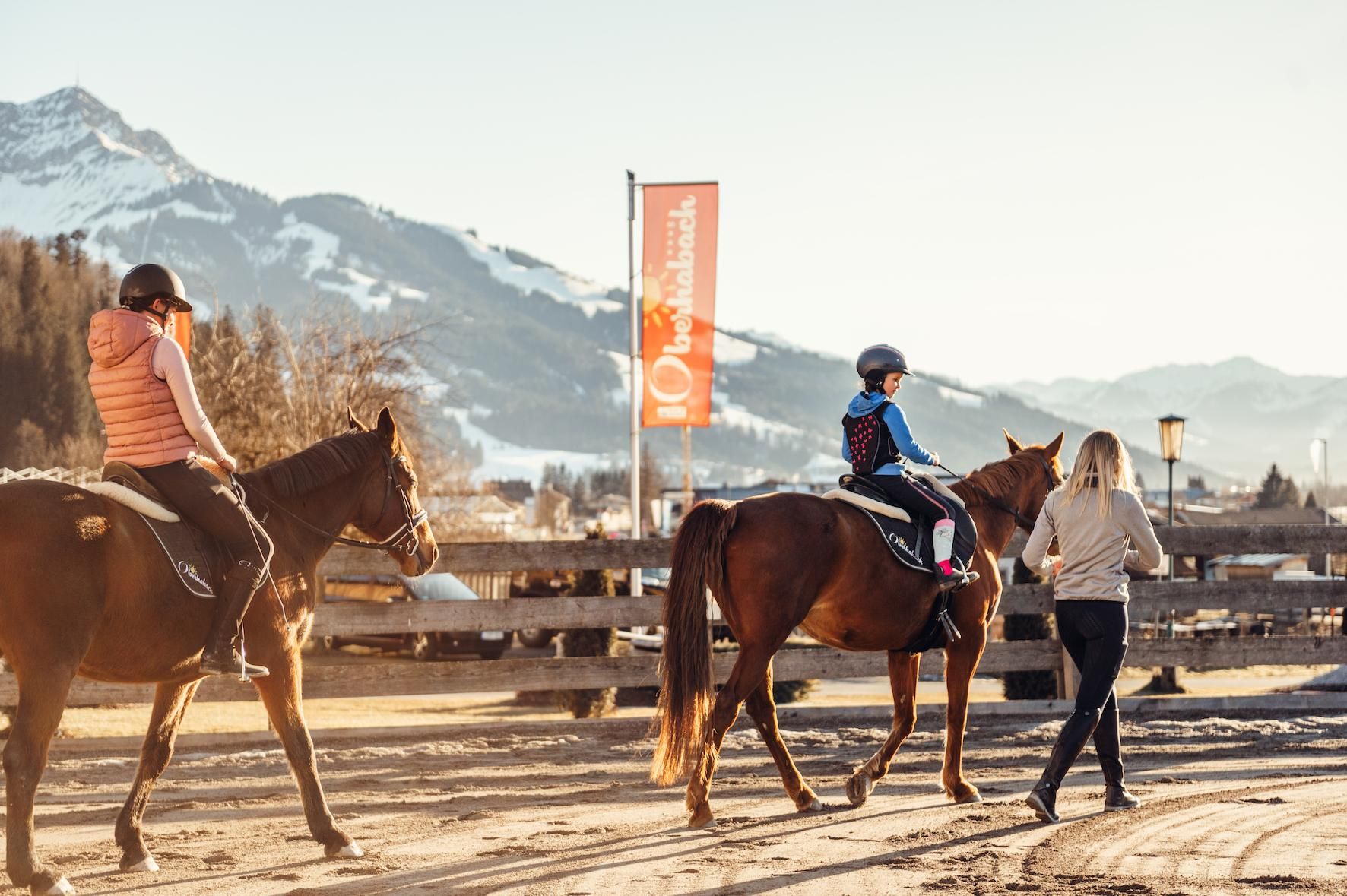 A riding boy and a girl on horses in a picturesque landscape. In the background, mountains and a banner are visible.