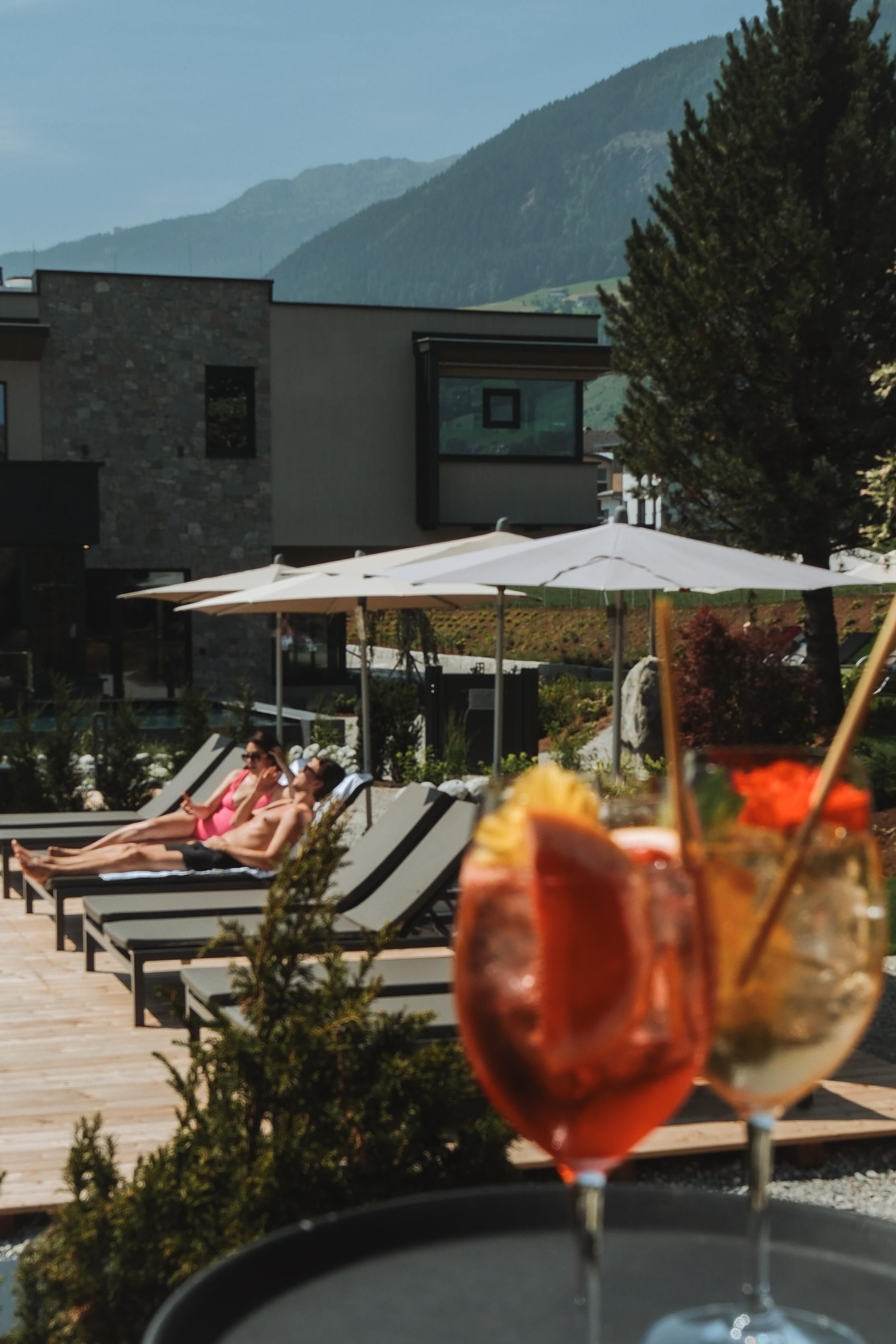 A relaxed outdoor area with loungers and sun umbrellas. In the foreground are two cocktails on a tray.