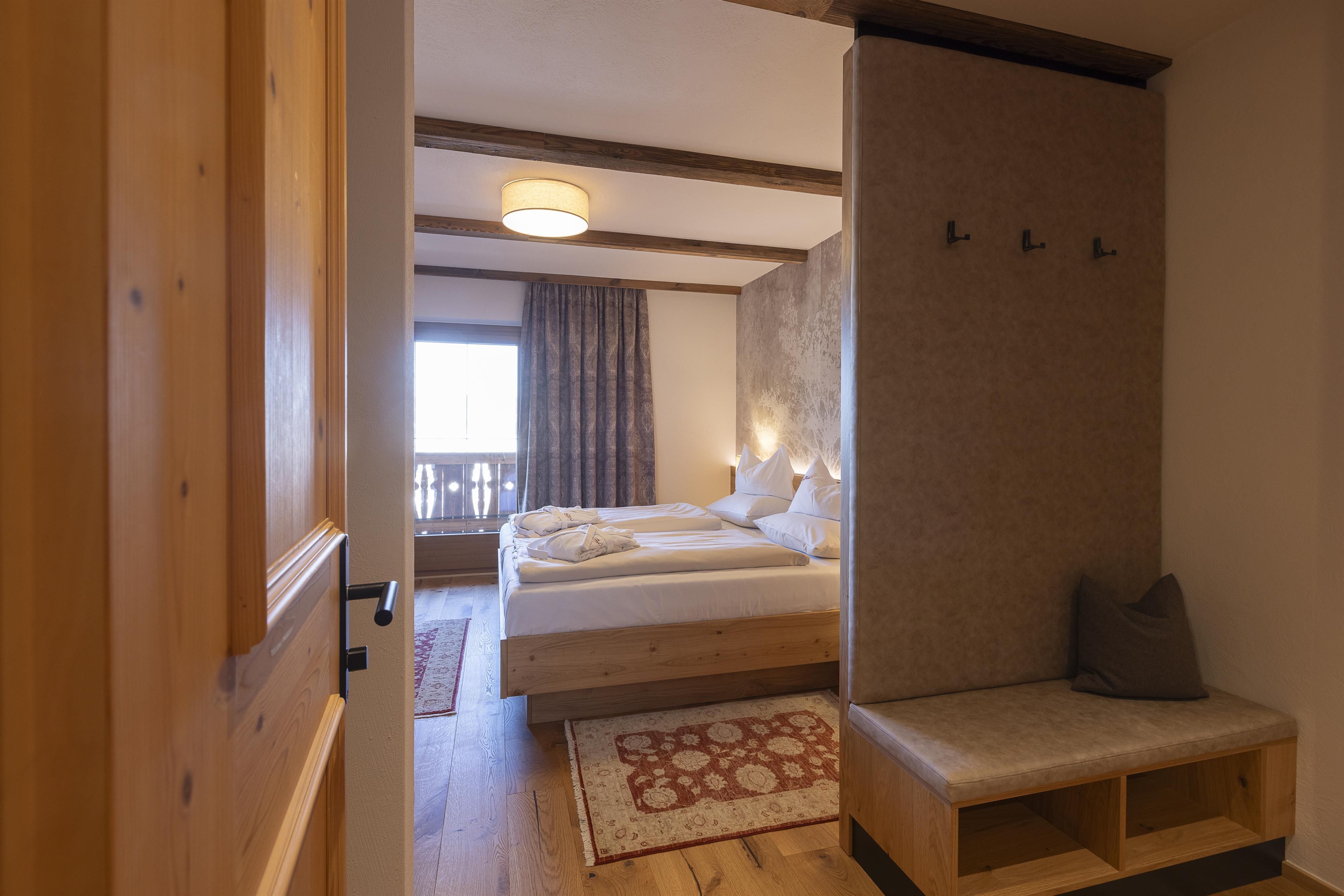 A cozy bedroom with a big bed and warm wooden elements. The windows offer a view of nature and provide plenty of daylight.
