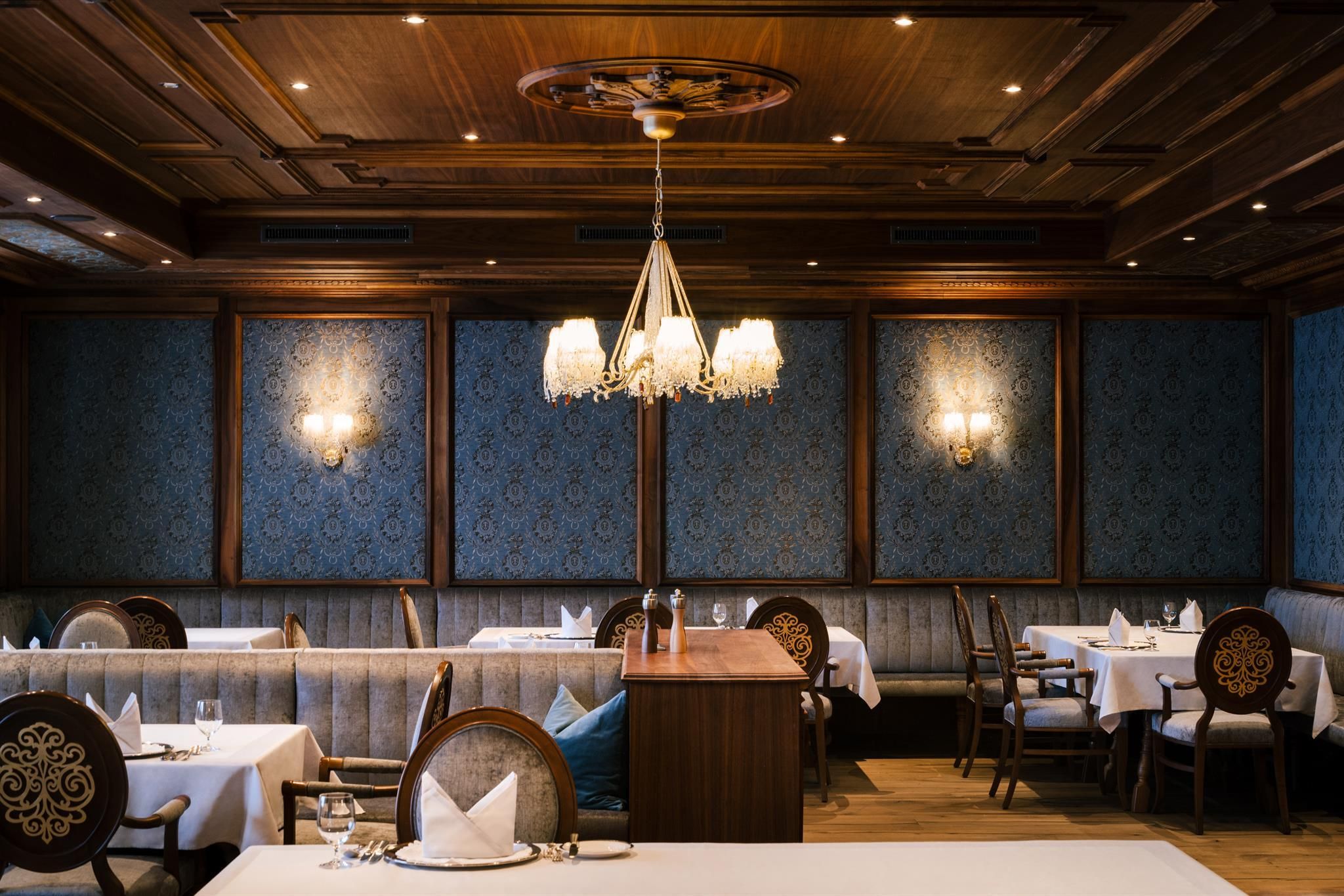 An elegant restaurant with stylish interiors and a warm lighting atmosphere. Tables are set with white tablecloths and dishes, surrounded by decorative walls.