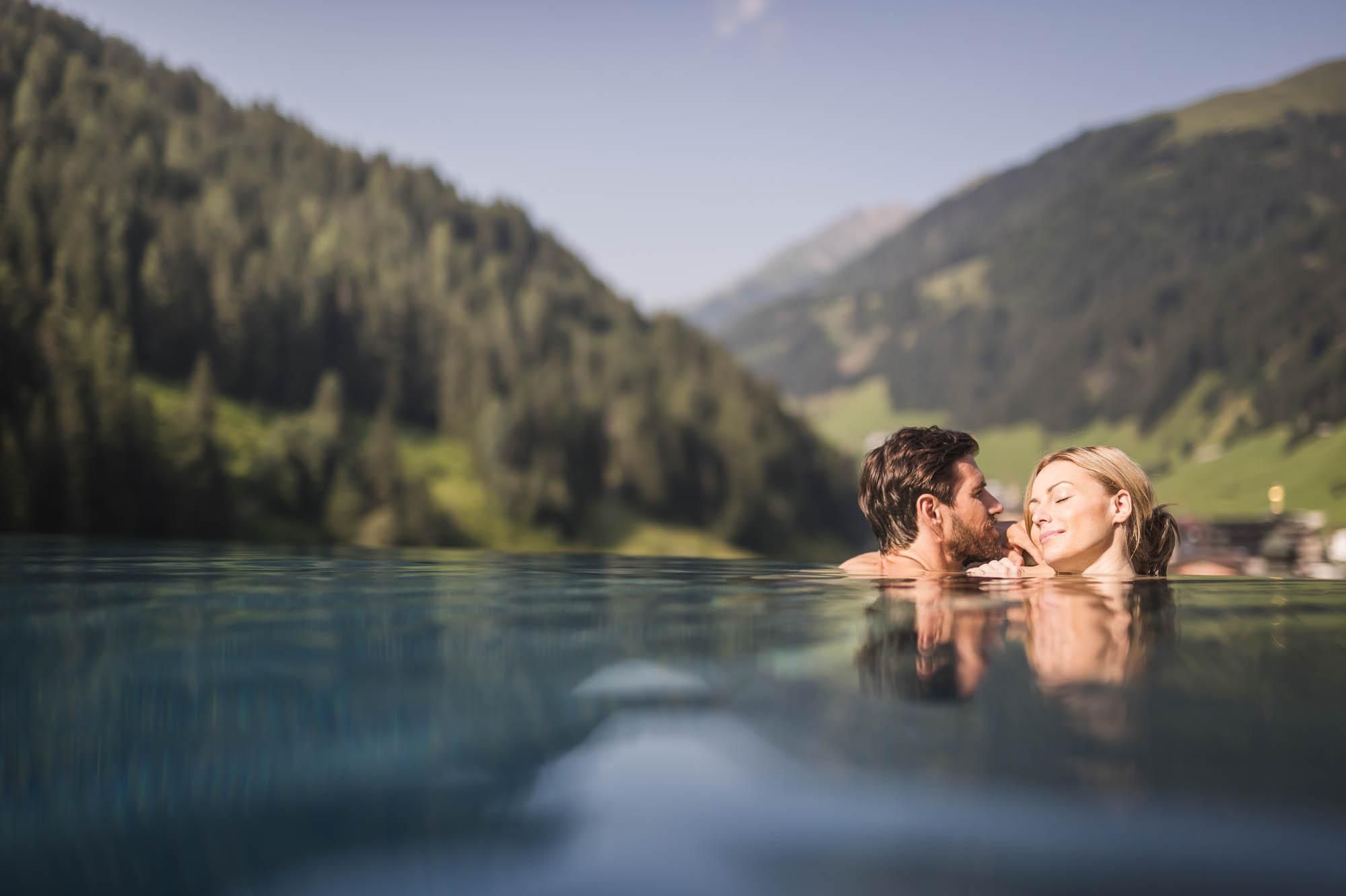 A couple enjoys a romantic moment in the water with a picturesque mountain landscape in the background. The mood is relaxed and loving.