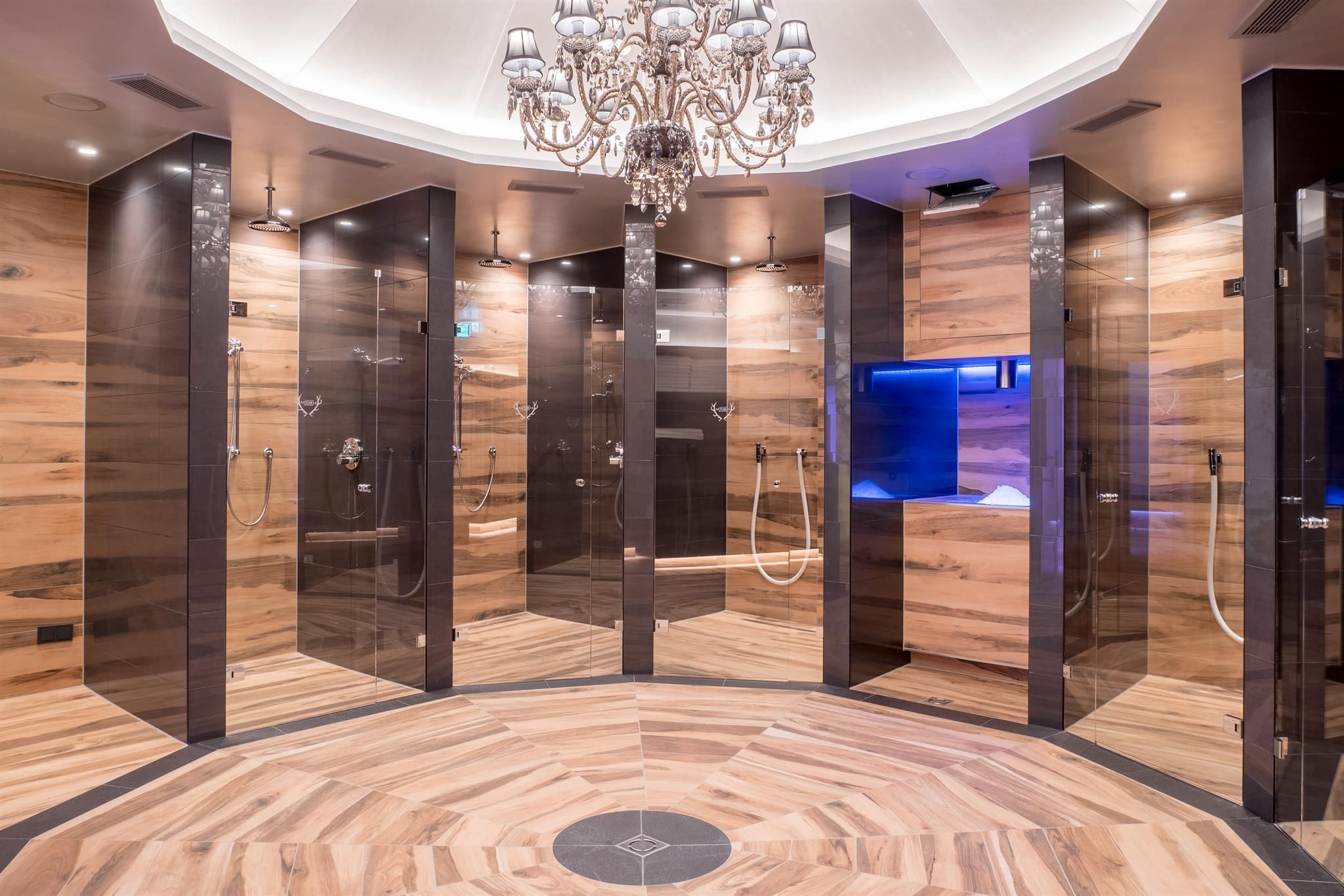 An elegant shower area with modern glass cabins and a stylish wooden floor. The lighting and chandelier give the space a luxurious atmosphere.