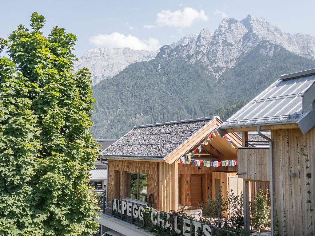 Wooden cabins in the Alps with a view of majestic mountains. The sky is clear and the surroundings are green and inviting.