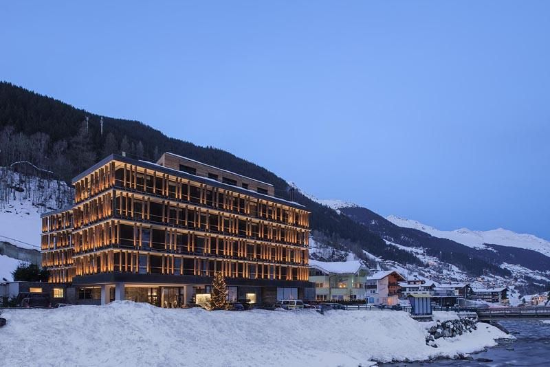 A modern hotel in a snow-covered landscape. The facade glows in the twilight.