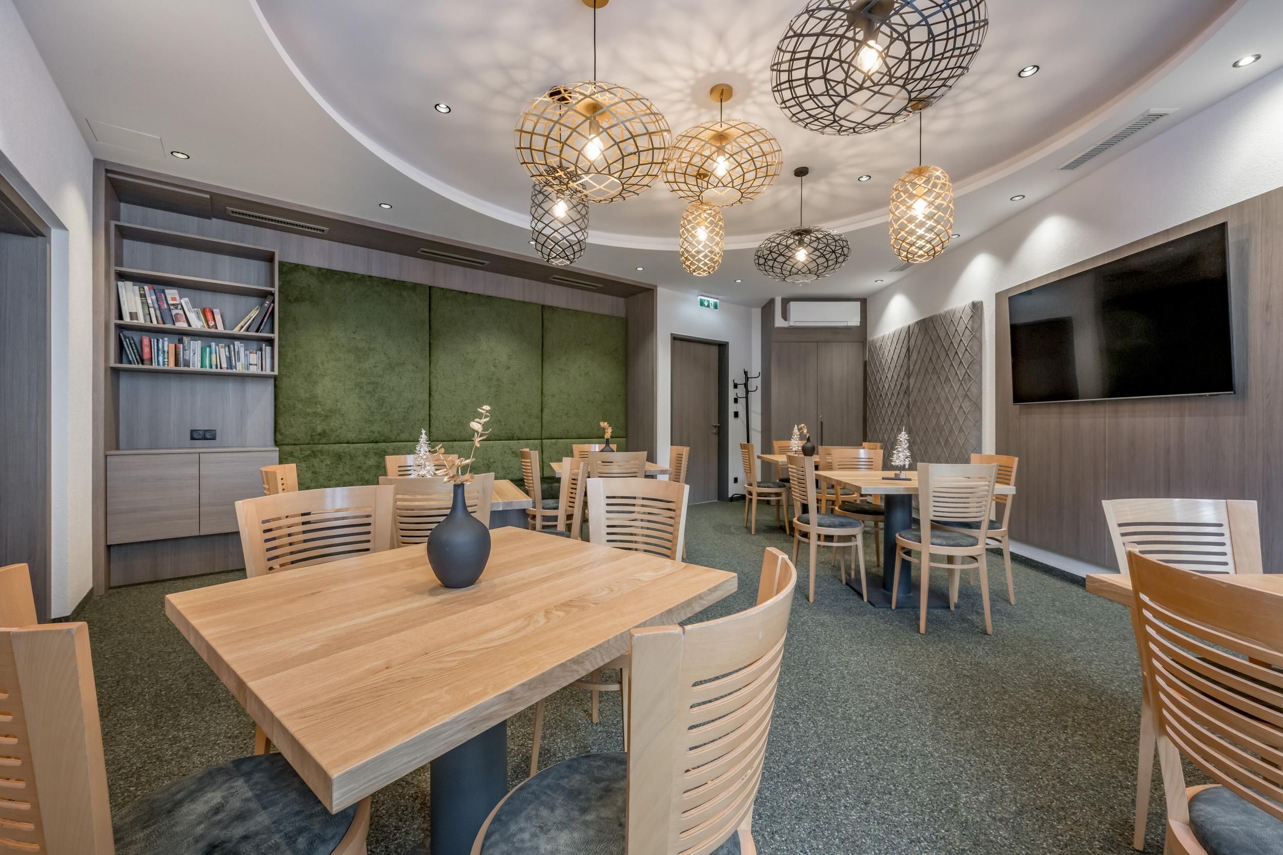 A modern interior with wooden tables and chairs.
Beautiful lamps hang from the ceiling and a green wall creates a cozy atmosphere.