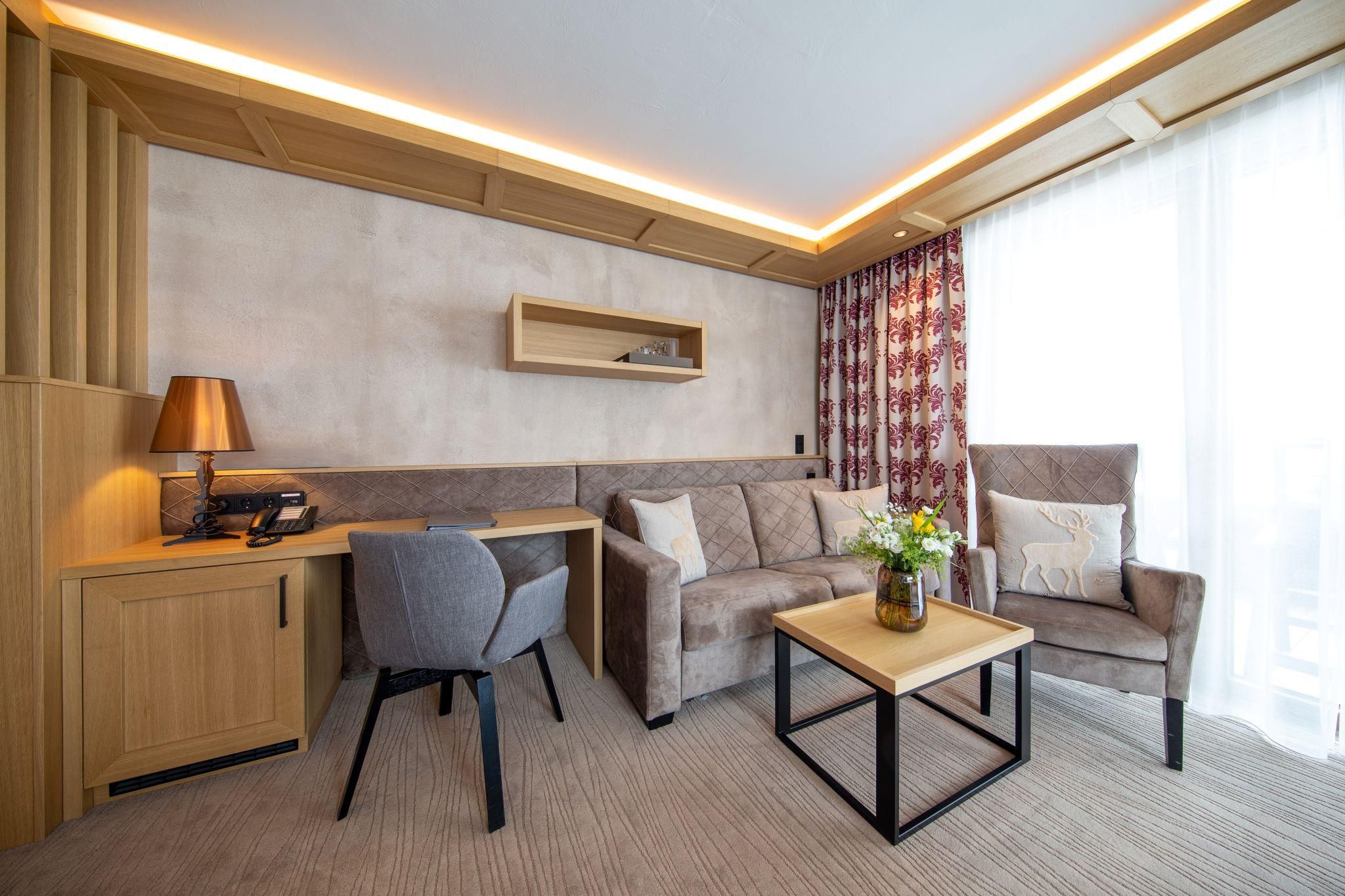 A modern living room with a cozy couch, an armchair, and a small table. Large windows allow plenty of daylight, and the decor is stylish and inviting.