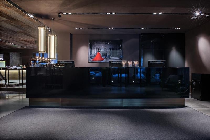 A modern hotel lobby with an elegant reception desk and stylish lighting. In the background, there is a piece of art featuring a red figure.