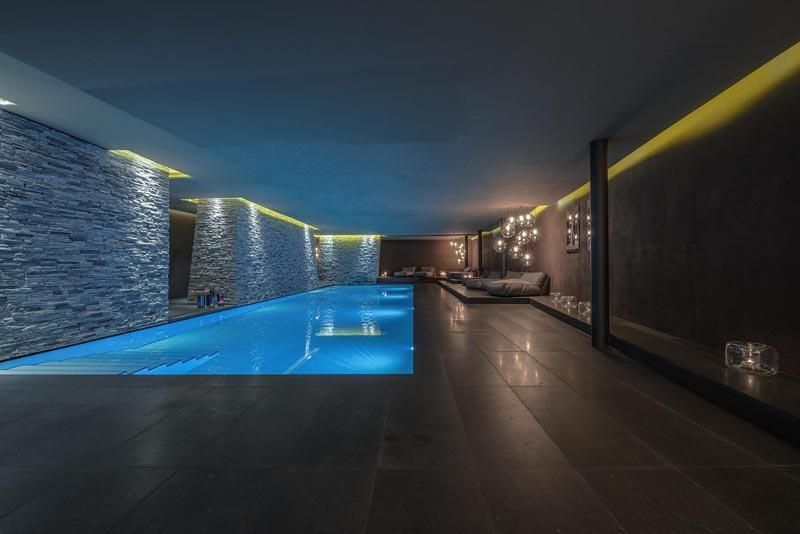 An elegant pool area with atmospheric lighting. The walls are clad with stone slabs, creating a tranquil atmosphere.