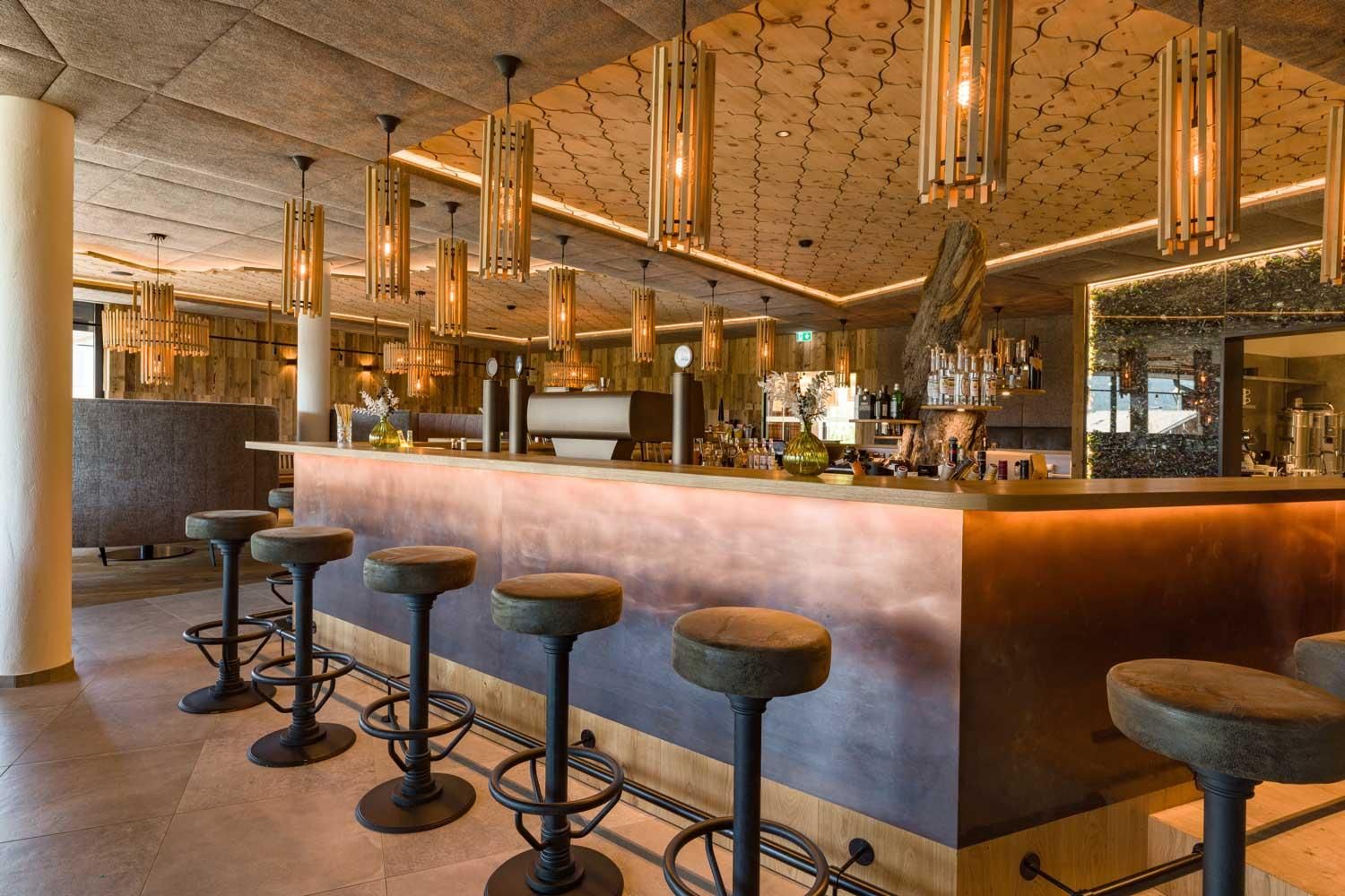 A modern bar with stylish stools and elegant lamps. The area is well-lit and invitingly designed.