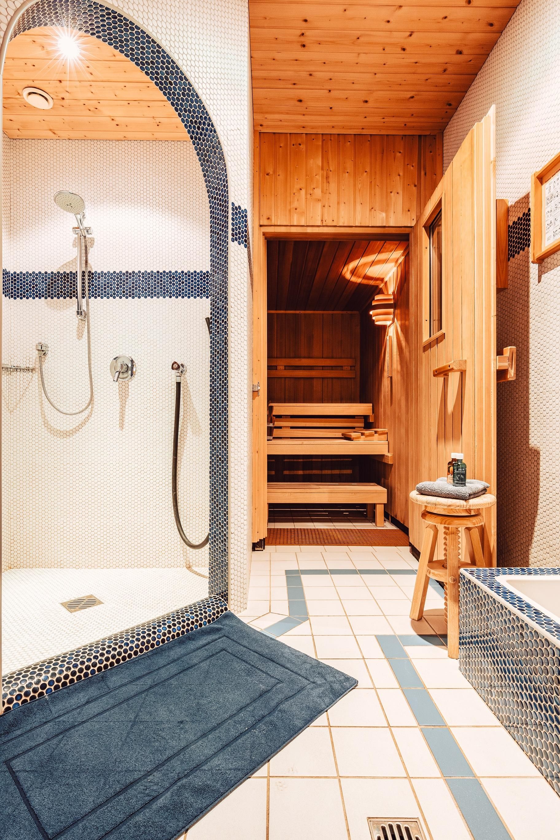 A modern bathroom with a shower and a sauna. The wooden ceiling and tiled floor create a relaxing atmosphere.