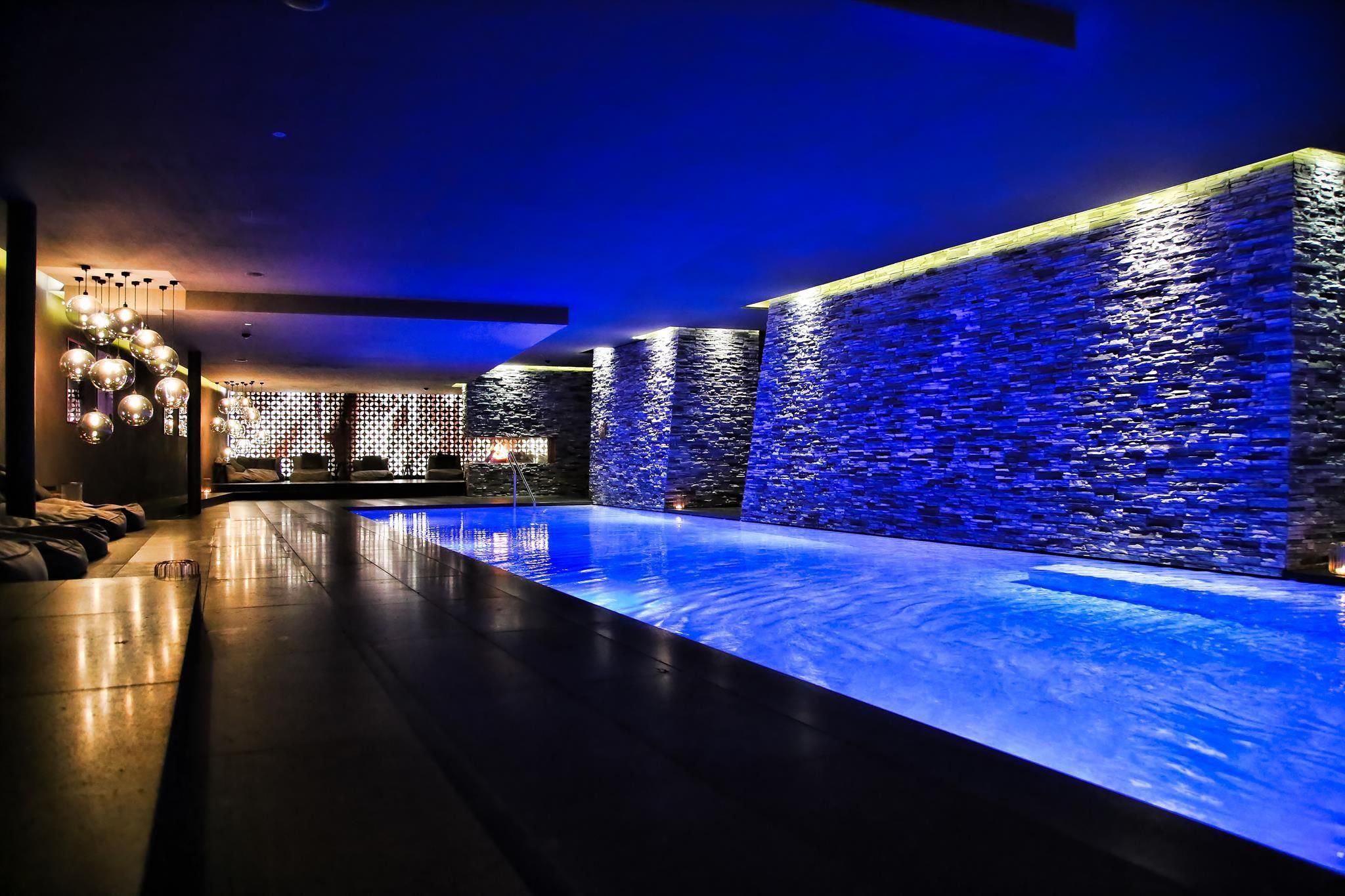 A stylish indoor pool with blue lighting and stone walls. The room feels modern and relaxing.