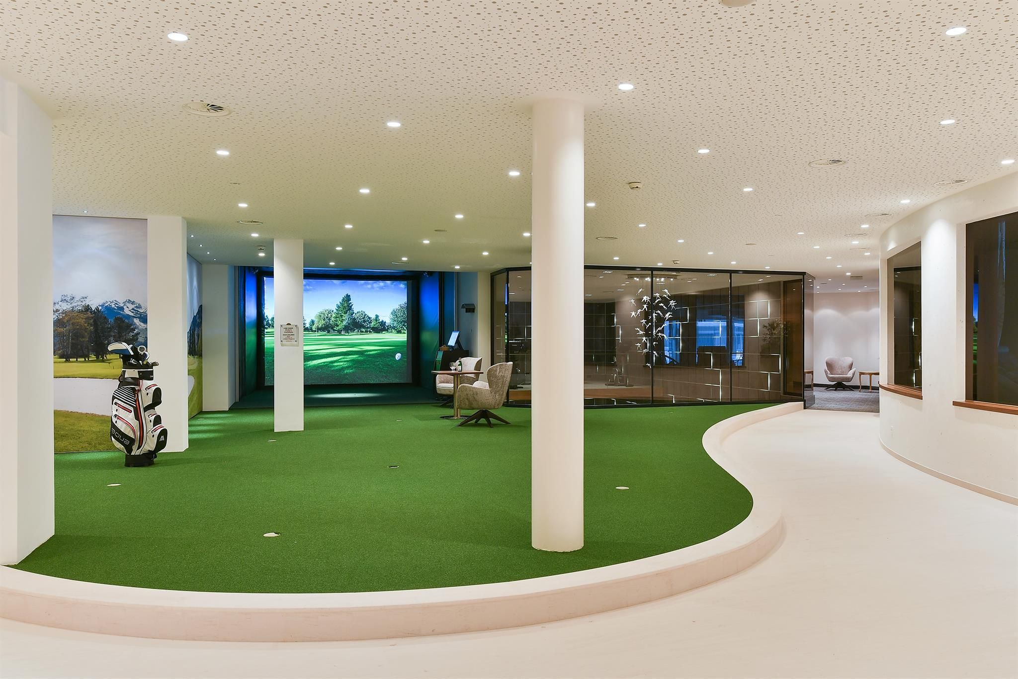 An elegant golf simulator room with green carpet and large screens. The room is modernly designed and offers space for golf training and leisure.