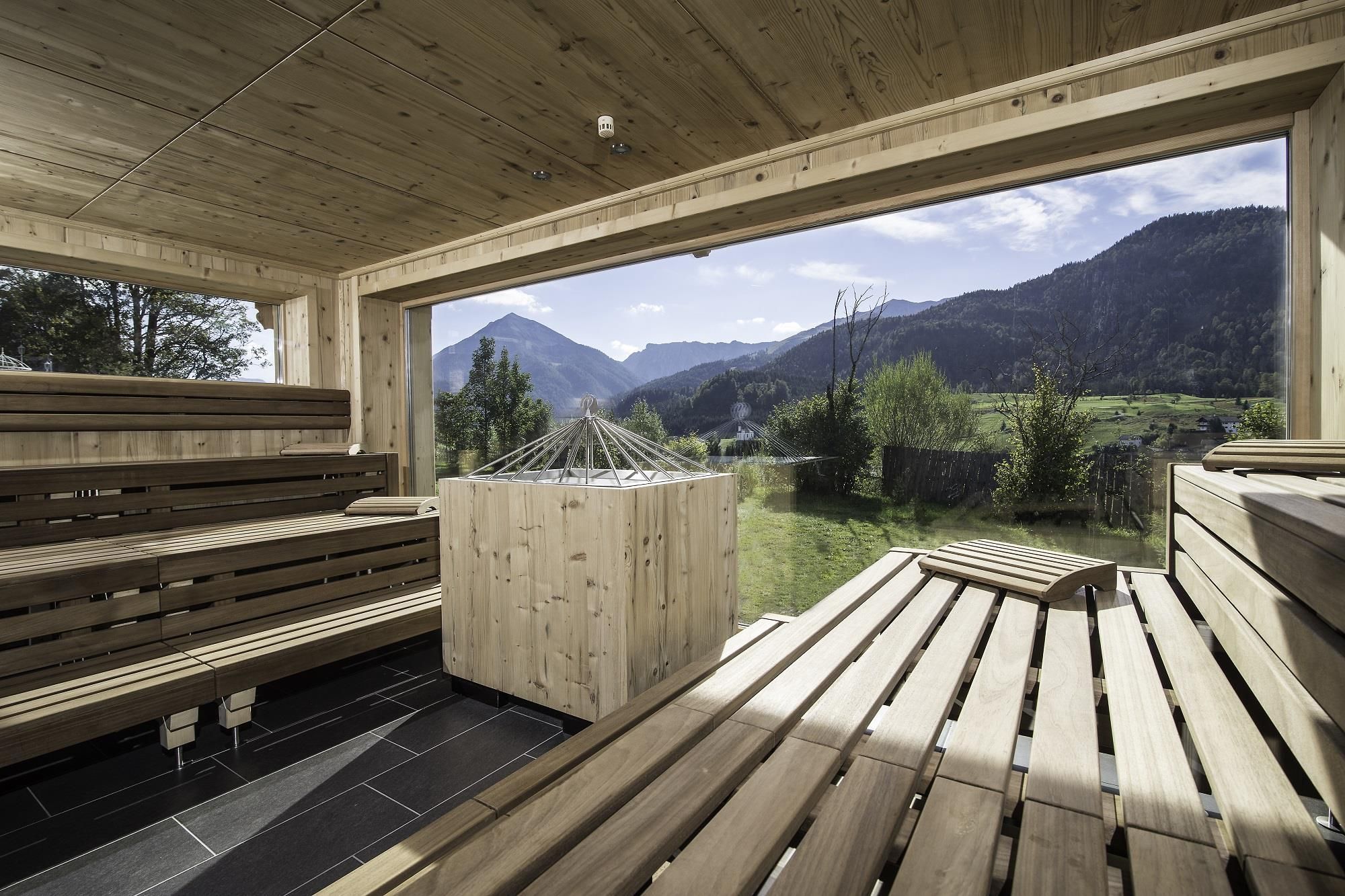 A modern sauna interior design with a wooden bench and windows that open up to the mountain view. The tranquil natural surroundings invite relaxation.