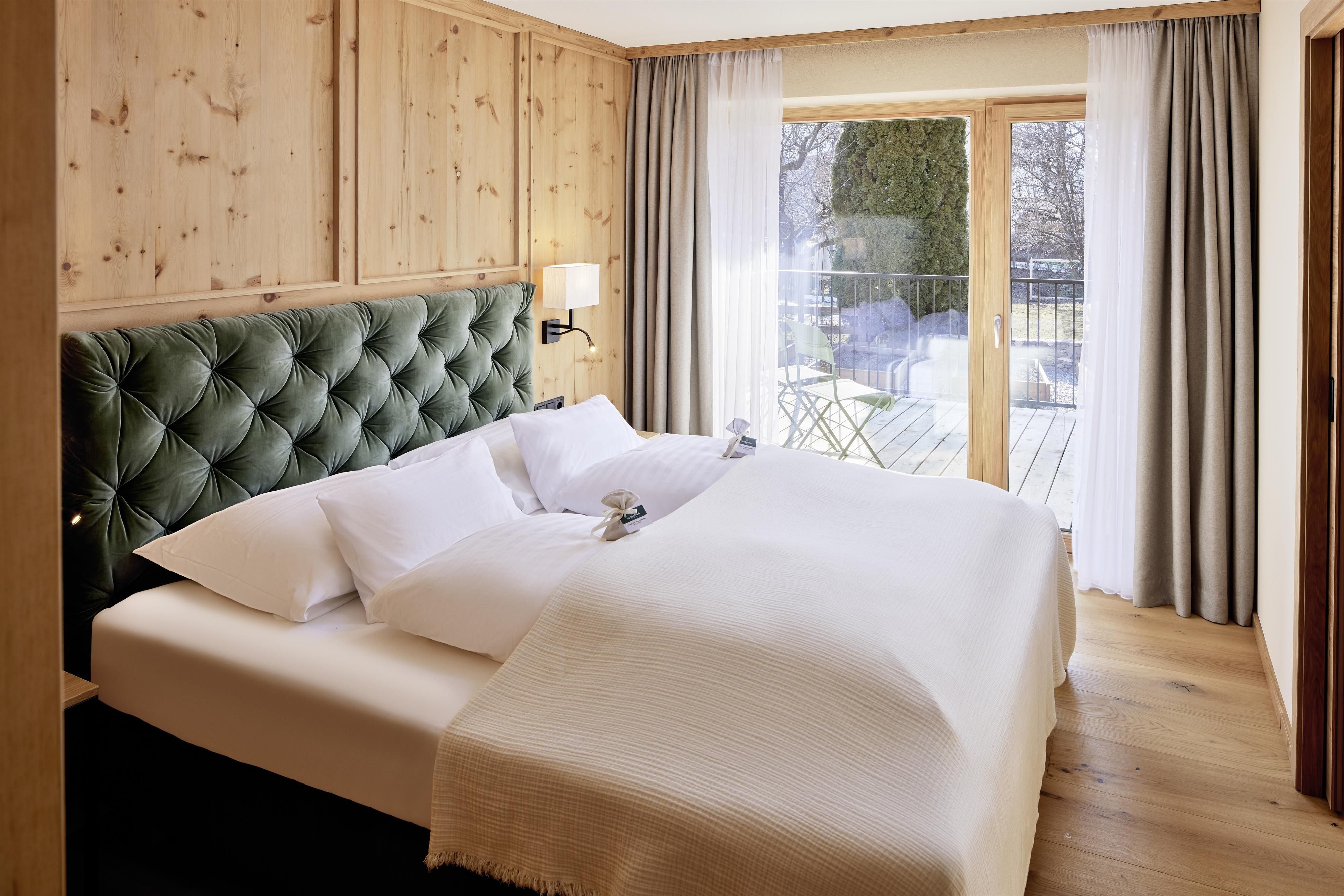 A cozy bedroom with a large double bed and an elegant headboard. Large French doors provide a view outside and let in plenty of light.