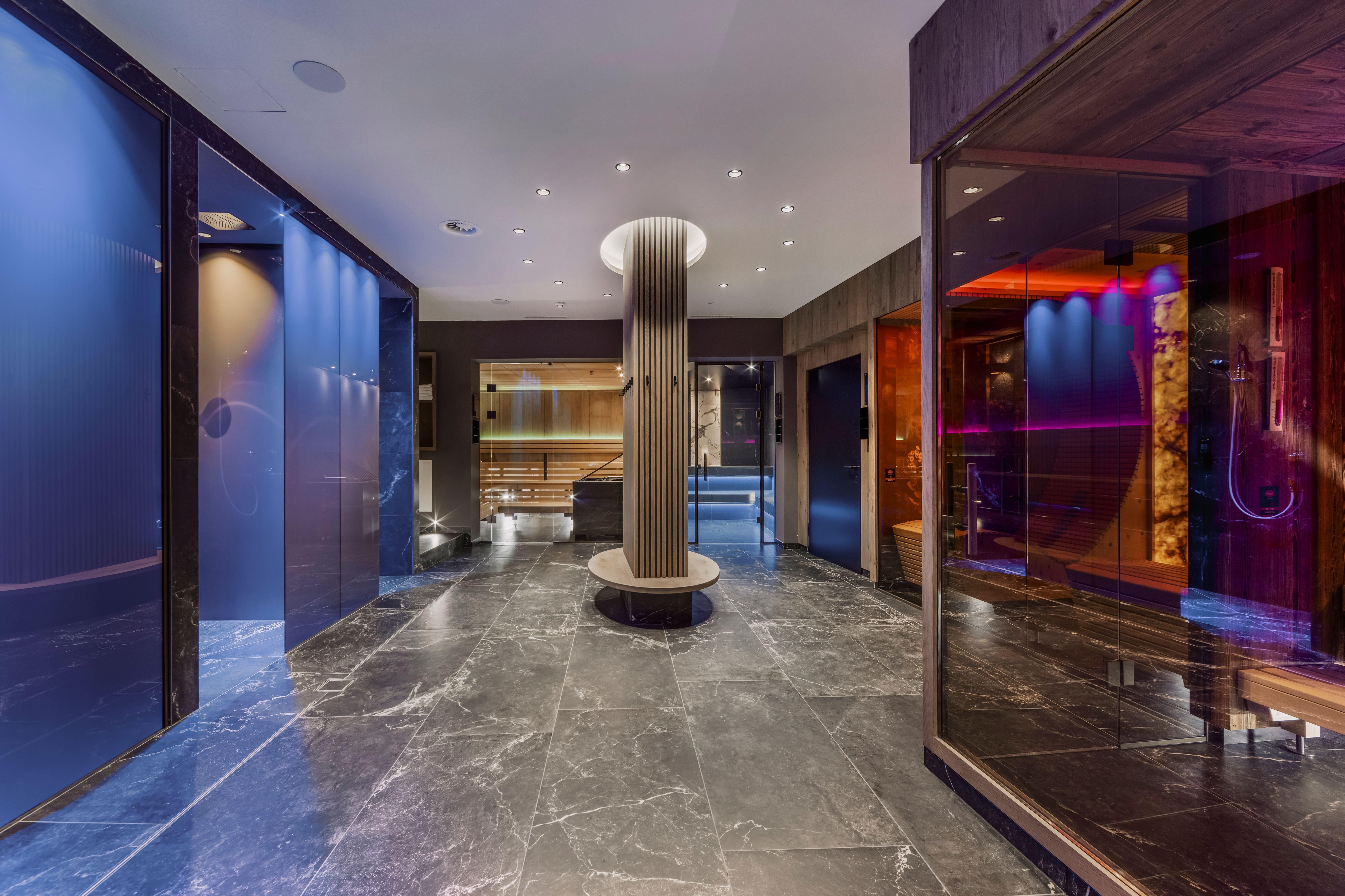 An elegant wellness area with modern saunas and a stylish reception area. The floor is made of dark marble and the walls shine in soft colors.