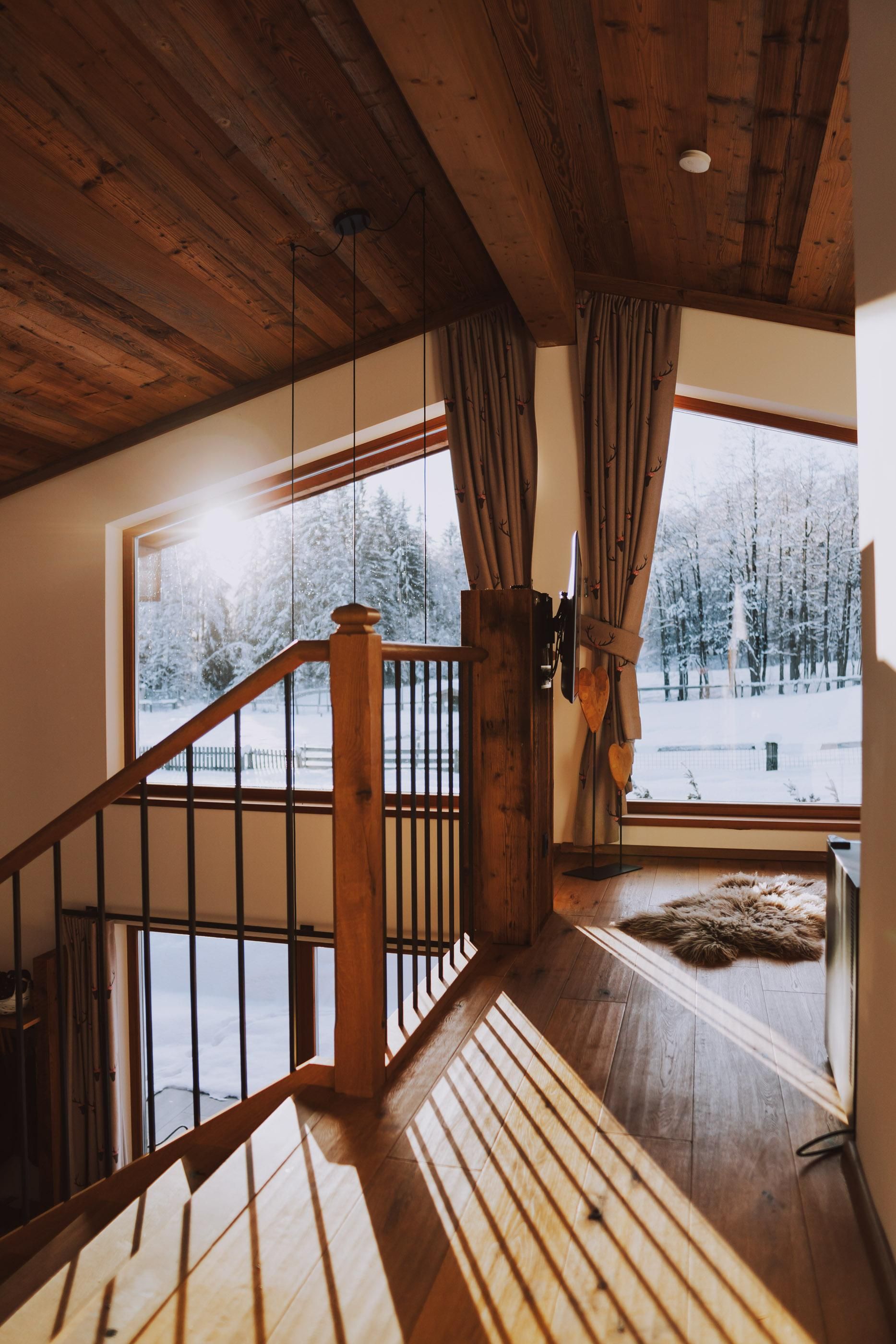 A beautiful interior with a wooden staircase and large windows. Outside, a snowy landscape can be seen.