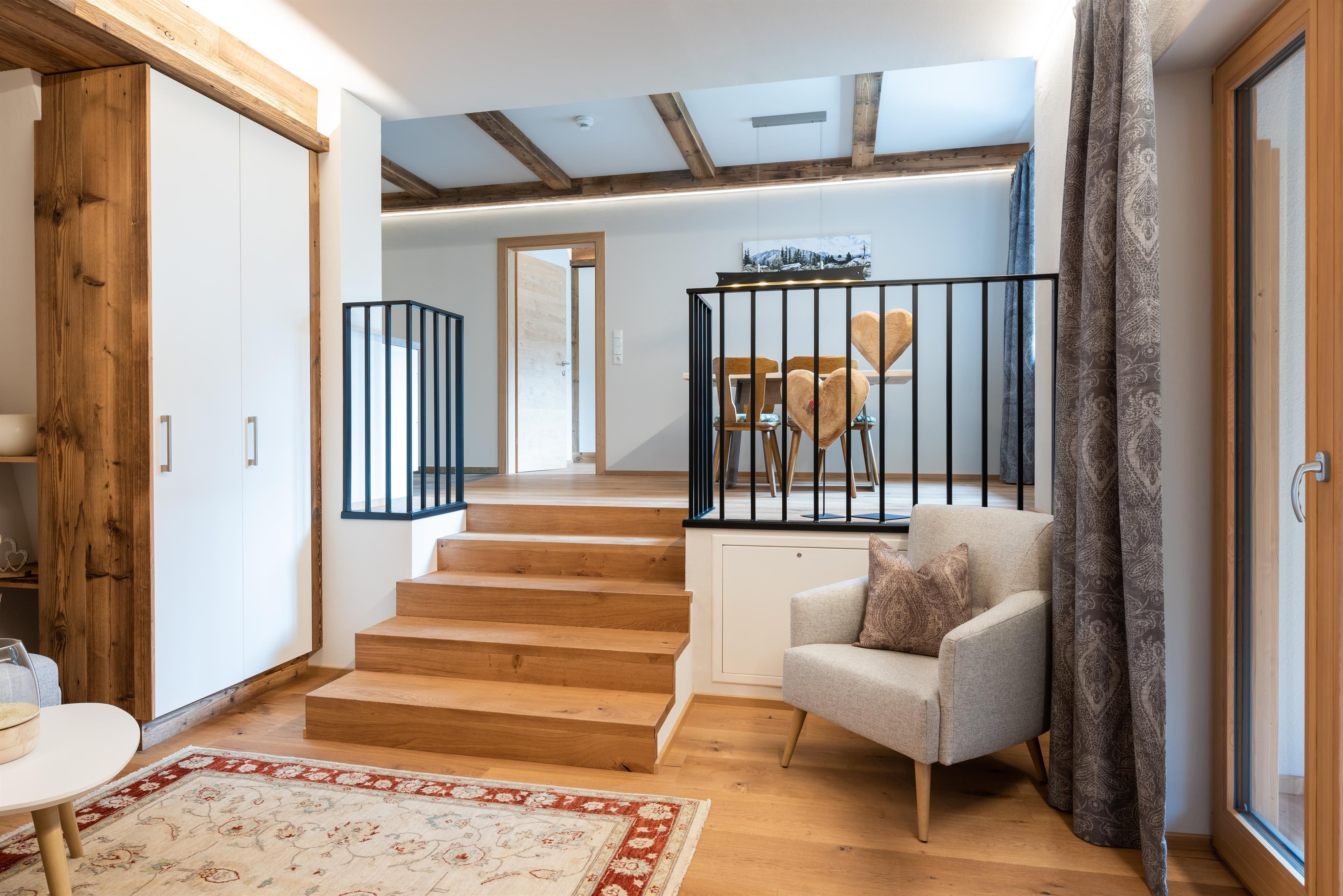 A modern living environment with wooden steps and a cozy armchair. In the background, there is a dining area with a table and chairs.