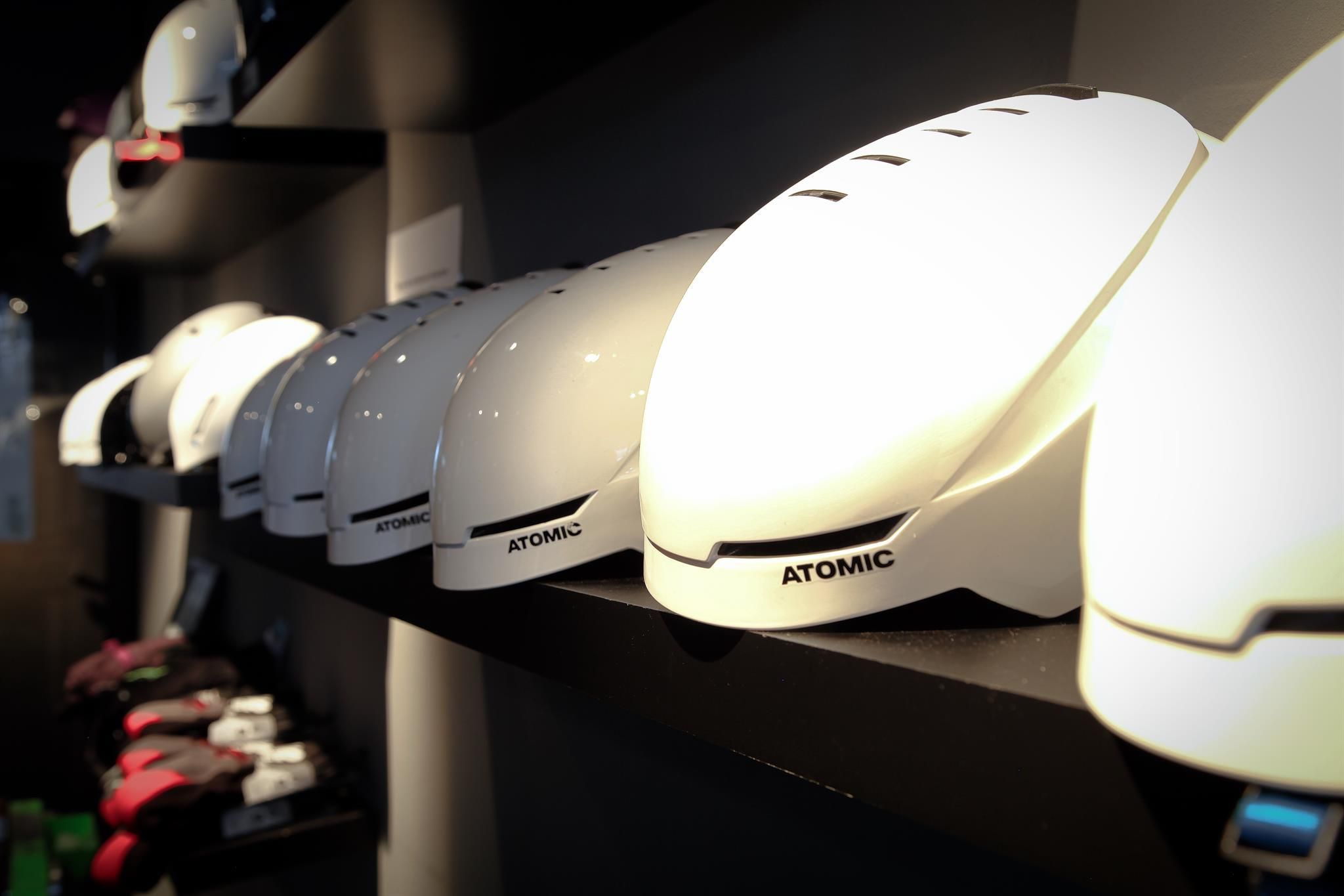Row of white helmets on a shelf. The helmets belong to the brand Atomic and are intended for sports activities.