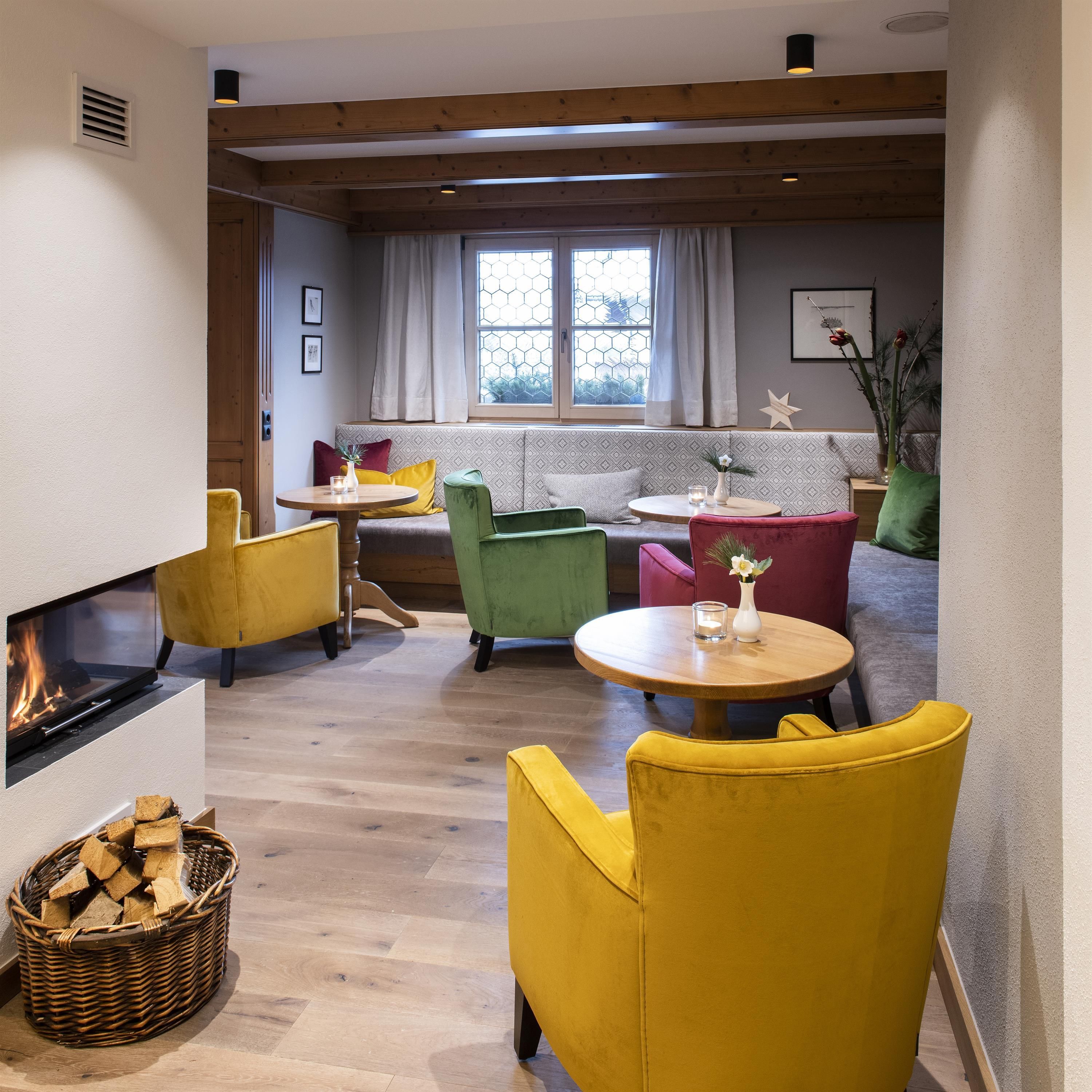 A cozy room with colorful chairs in yellow and green.
By the window stands a small table with a flower and an open fireplace creates an inviting atmosphere.