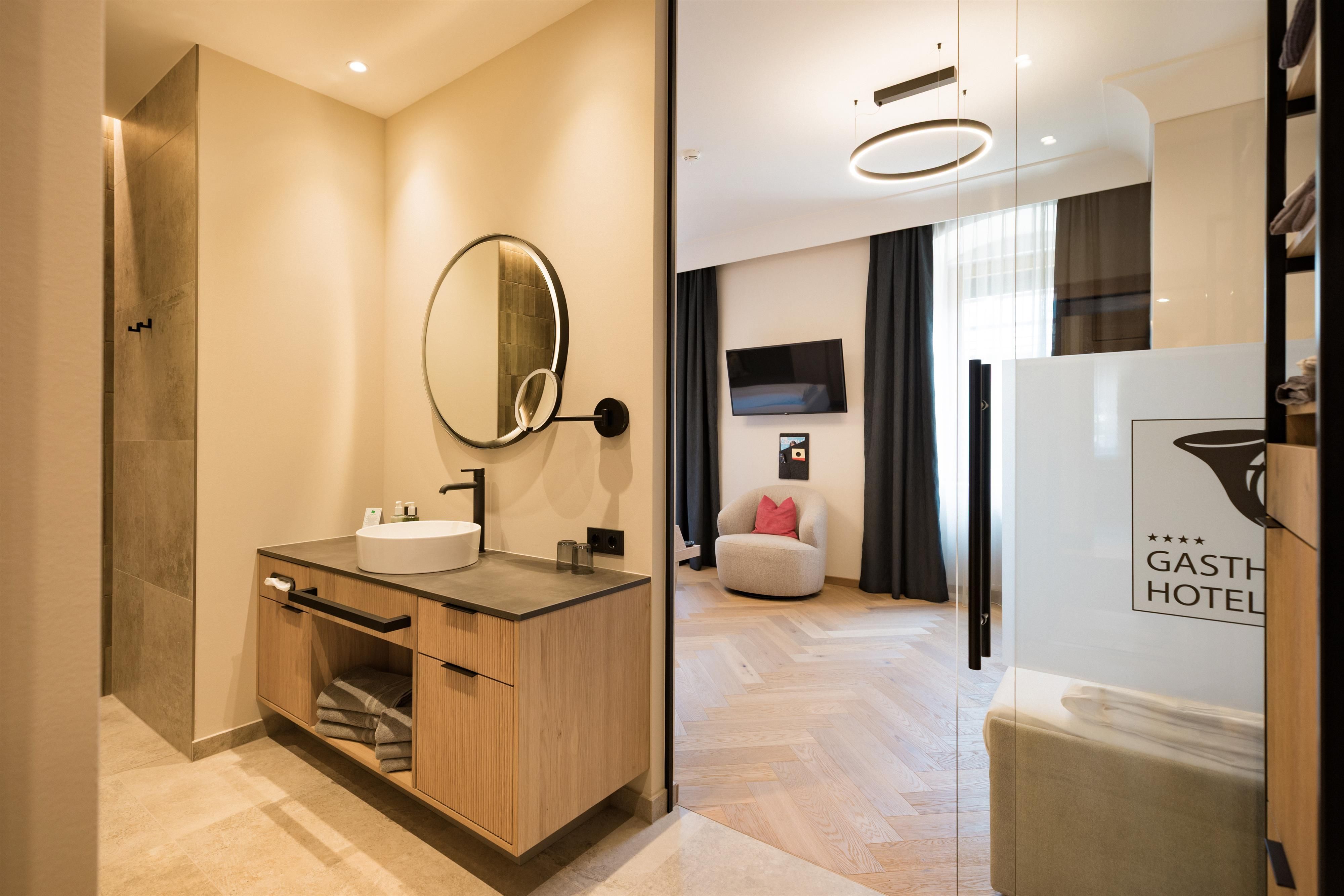 A modern bathroom with a sink and a large mirror. The space is bright and minimalist, overlooking a cozy living area.
