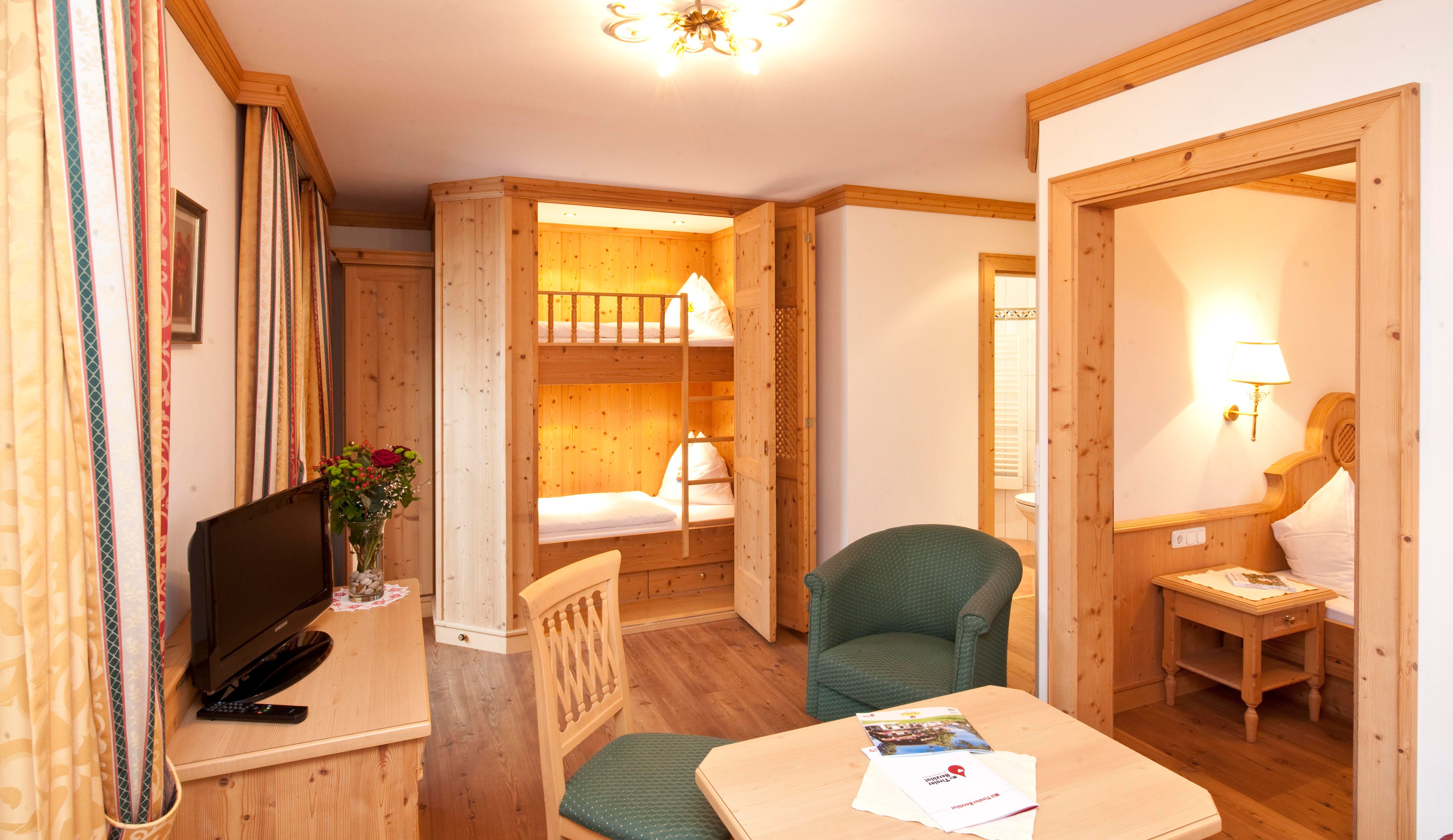 A cozy room with wood paneling and a seating area. In the background, there is a bunk bed for children.