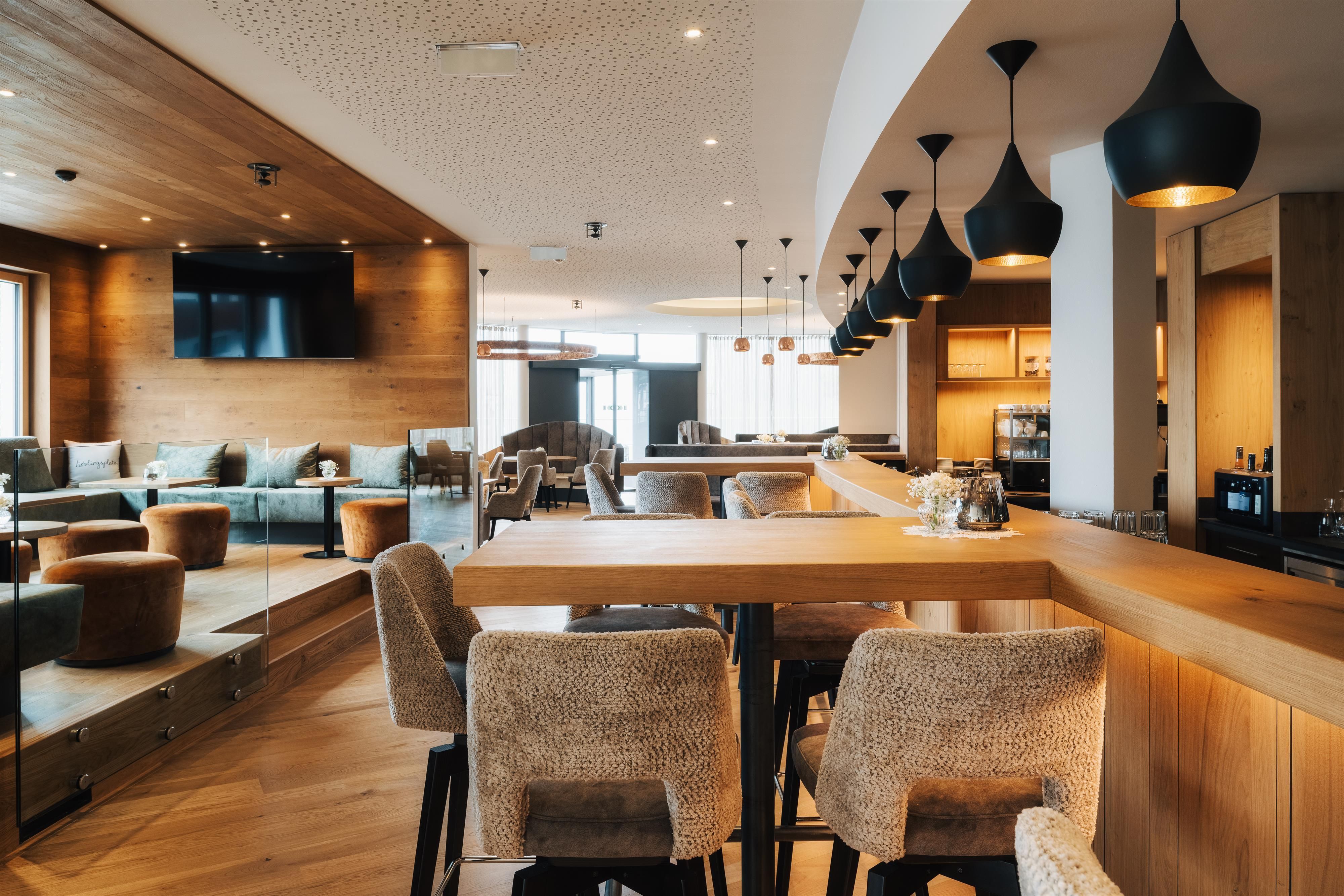 A modern bar with wooden decor and stylish lights. Cozy seating invites you to linger.