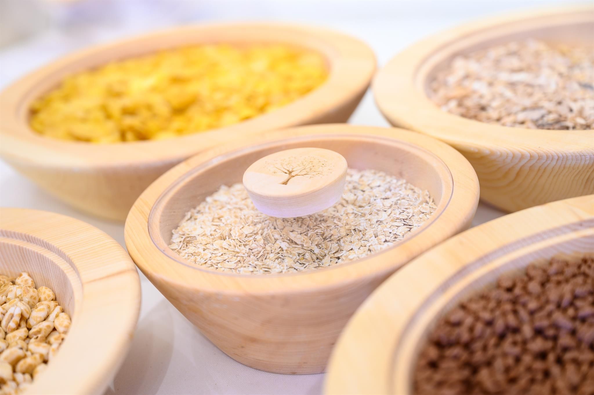 A selection of various grains in wooden bowls. Oatmeal, muesli, and other grains are displayed appetizingly.