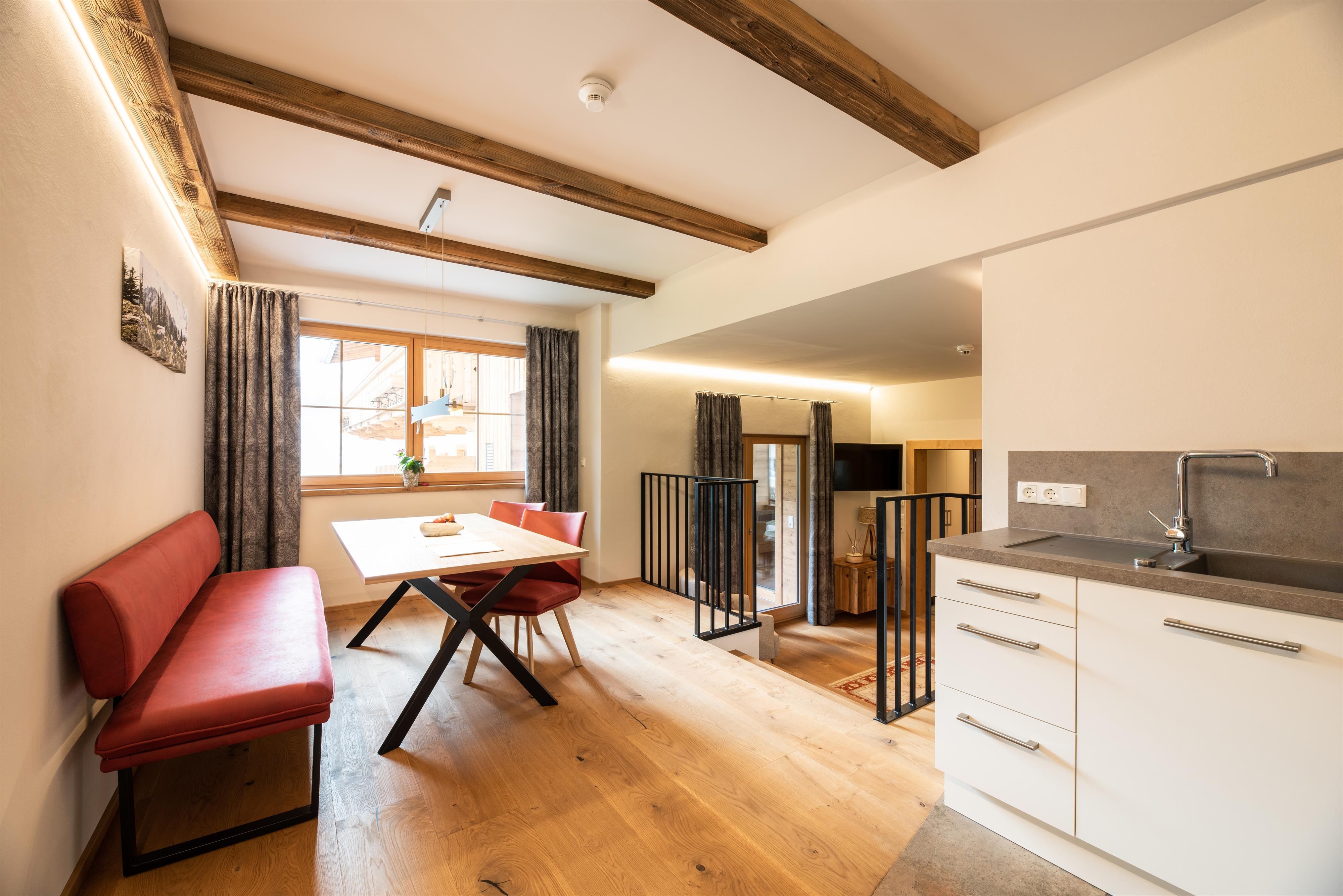 A modern living environment with wooden flooring and a dining area. The kitchen is open and bright, with a large window that lets in natural light.