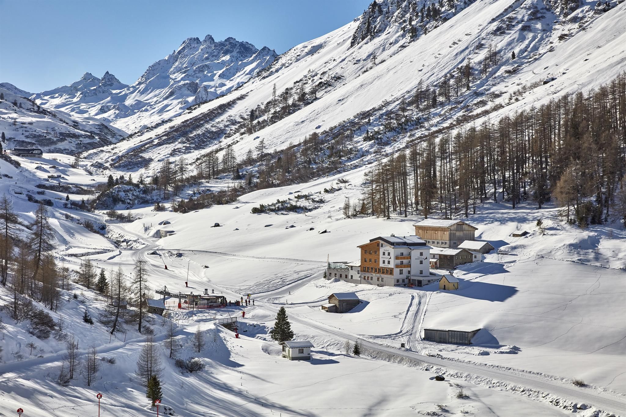 A picturesque winter landscape with snow-covered mountains and a small village. The clear air and the rays of sunlight give the scene a peaceful atmosphere.