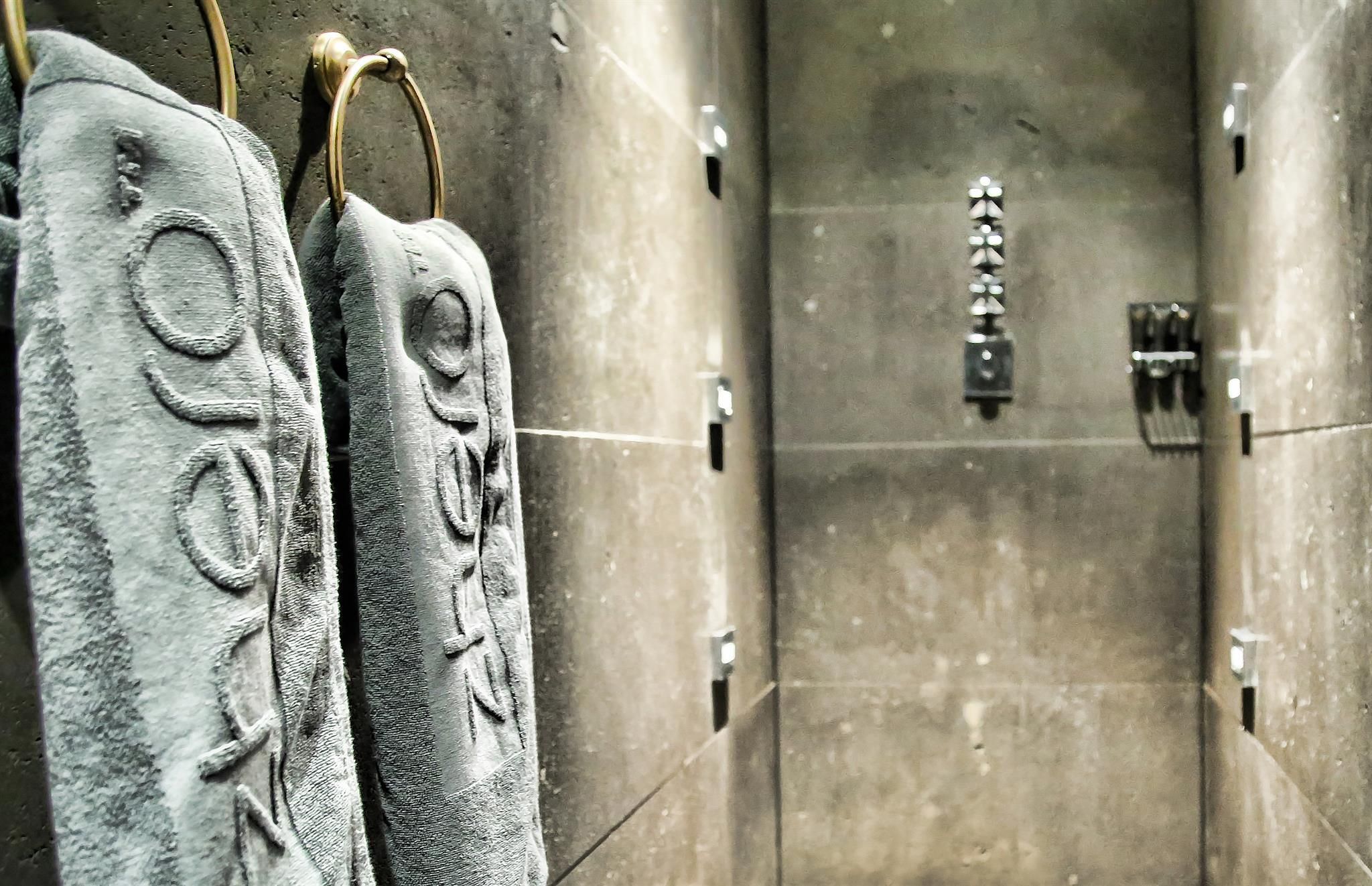 A modern bathroom with gray towels on a towel rack. The walls are done in a simple, dark stone.