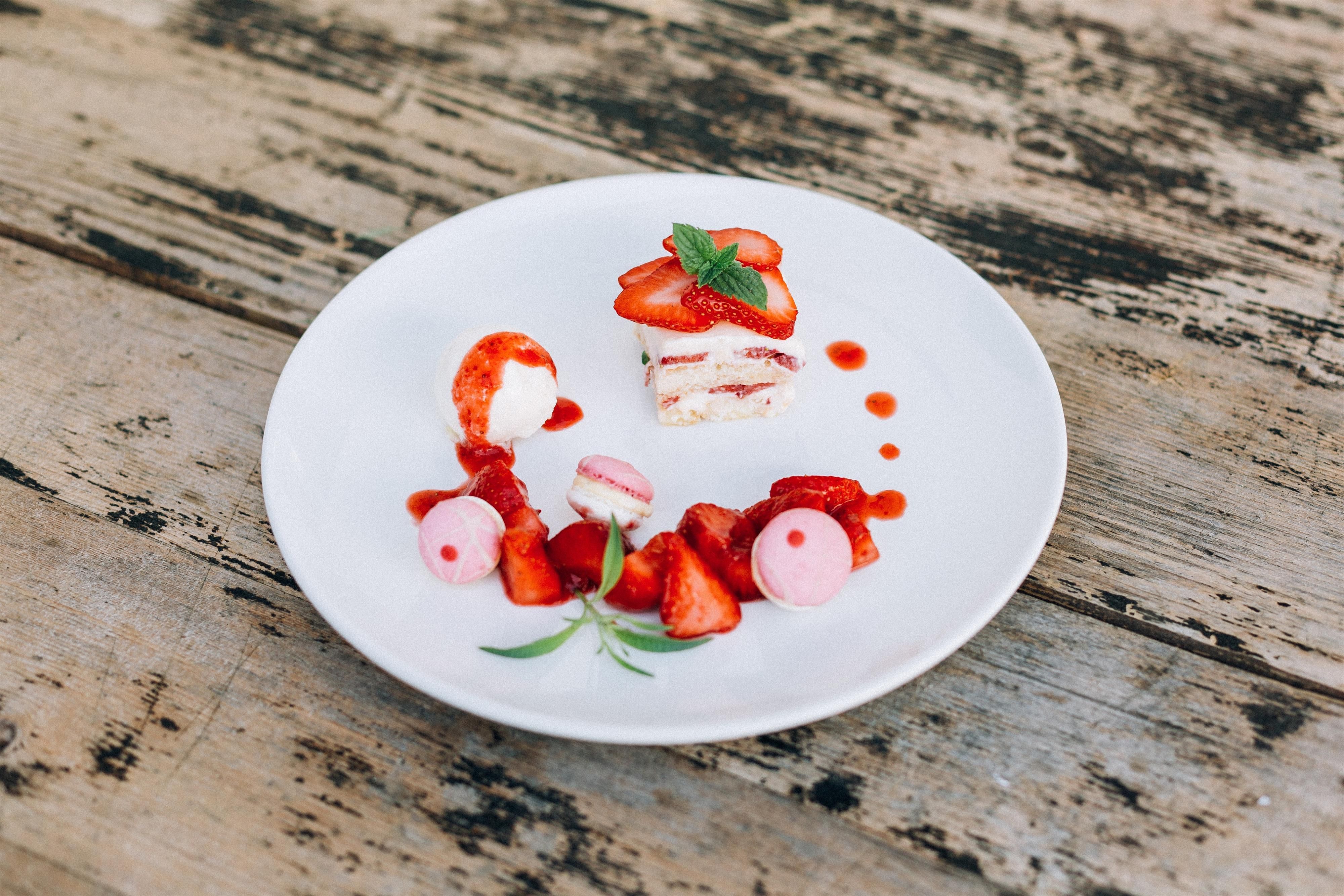 A plate with delicious dessert made of layers of cream and strawberries. Surrounded by fresh strawberries and a red sauce.
