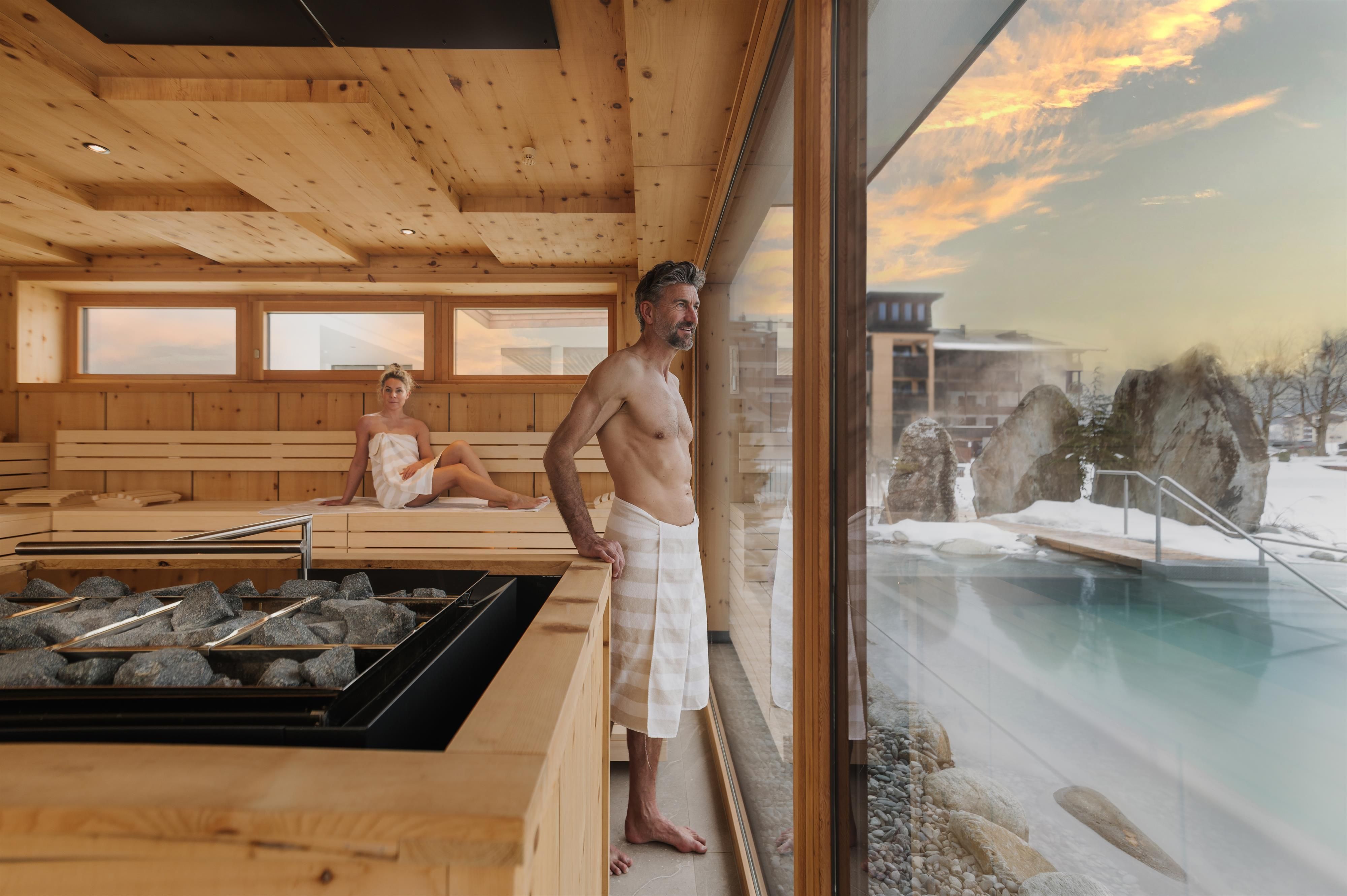 A relaxing wellness area with a sauna and a view of an outdoor pool. Two people enjoy the peaceful atmosphere.