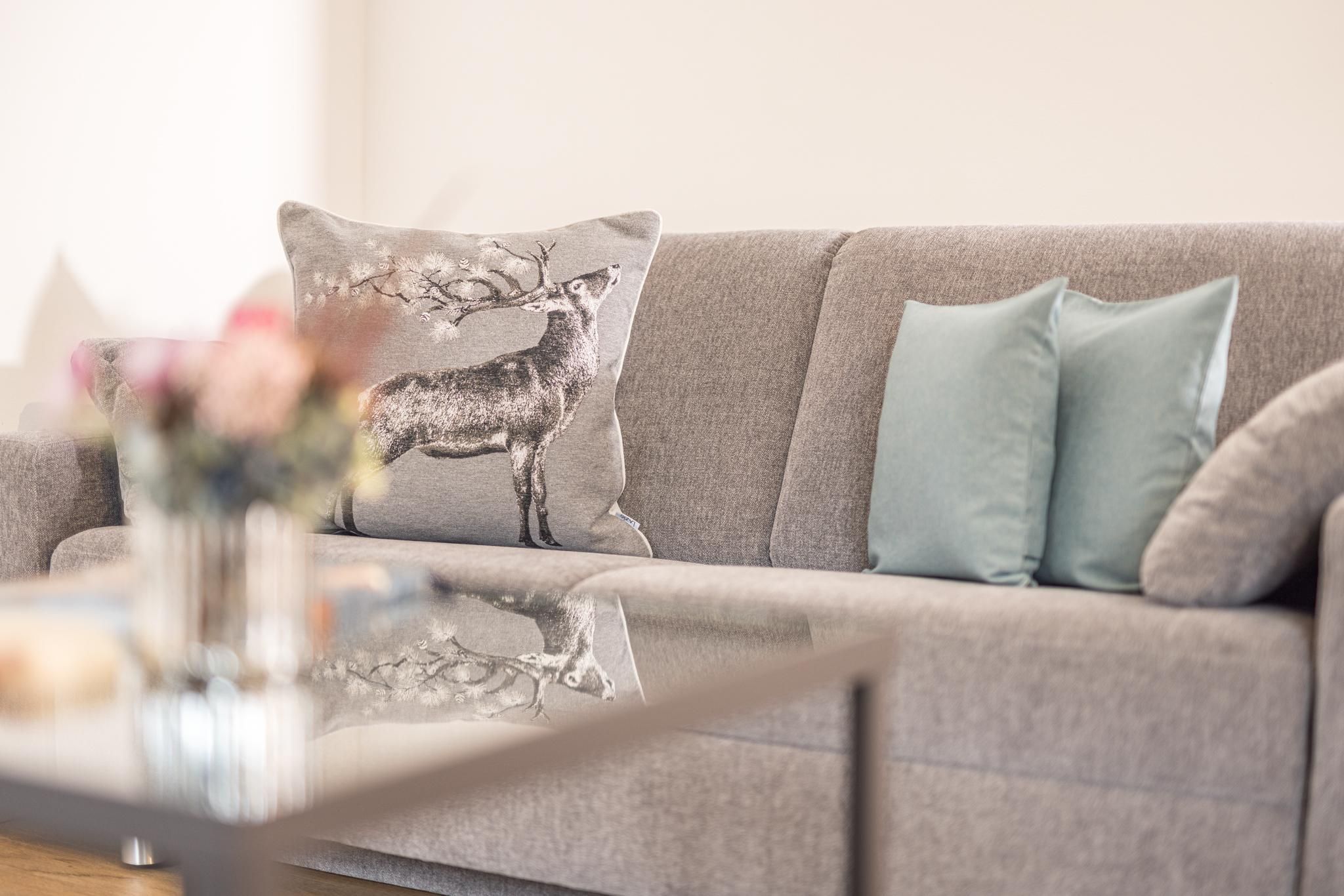 A bright living room with a gray sofa and decorative cushions. A flower vase sits on the table, refreshing the ambiance.